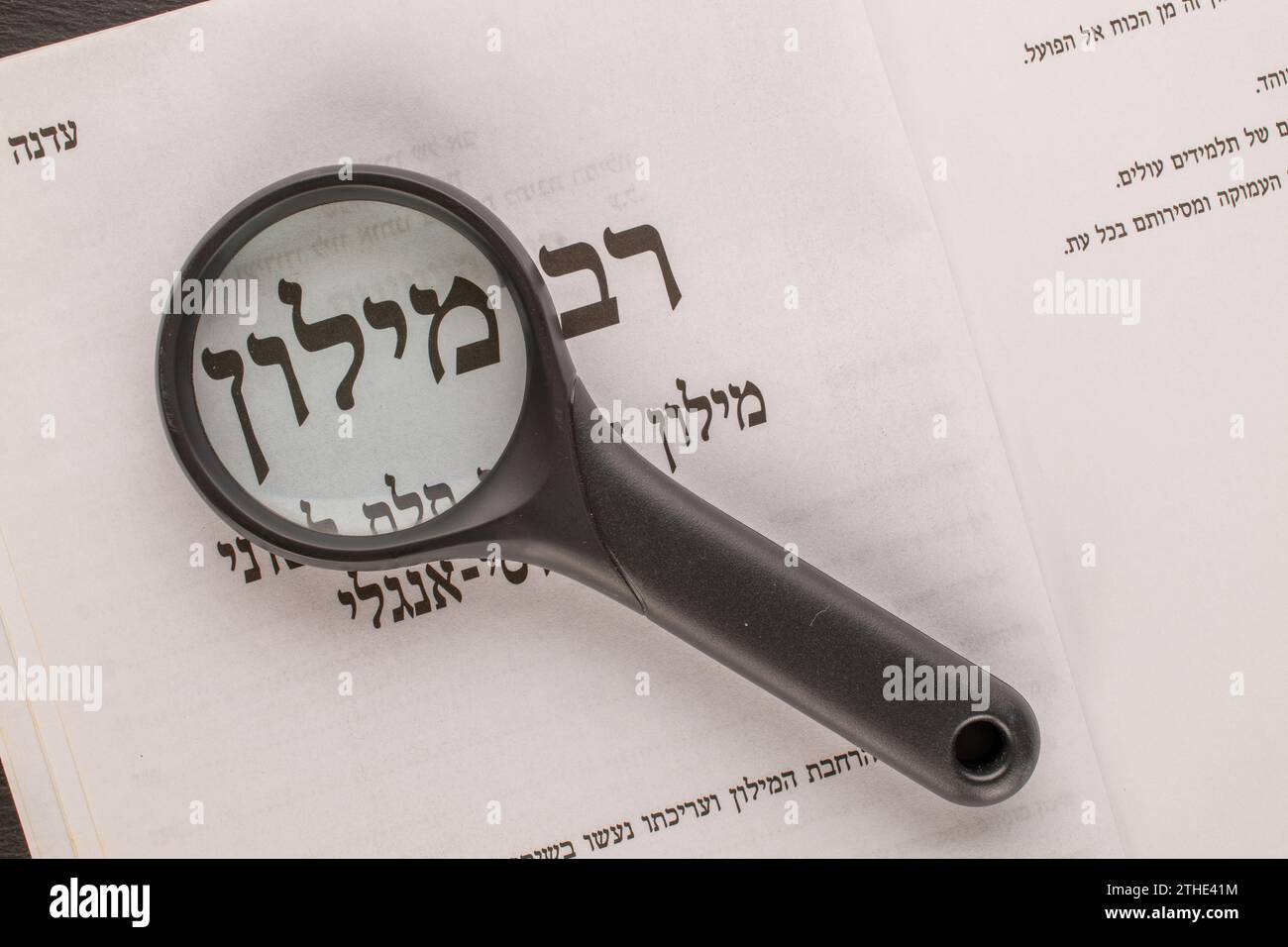 One magnifying lens on a Hebrew dictionary page, macro, top view. "The