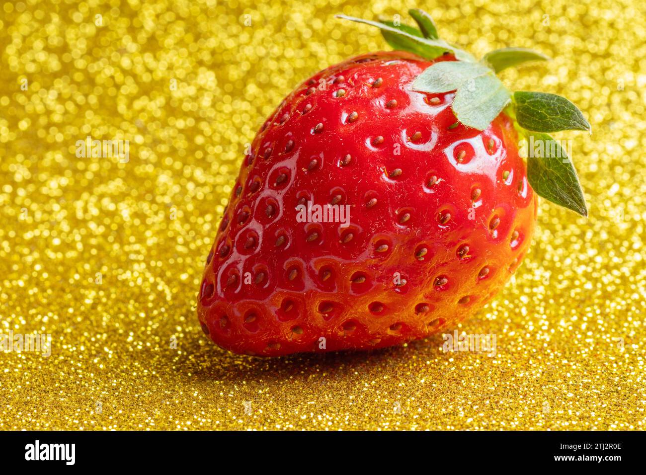 Red ripe strawberries with green leaves on a shiny yellow gold ...
