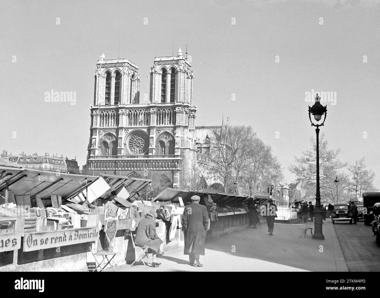 Paris. Bookstalls along the Seine with a view of the west facade of Notre Dame Cathedral and a street lamp ca. 1937 Stock Photo