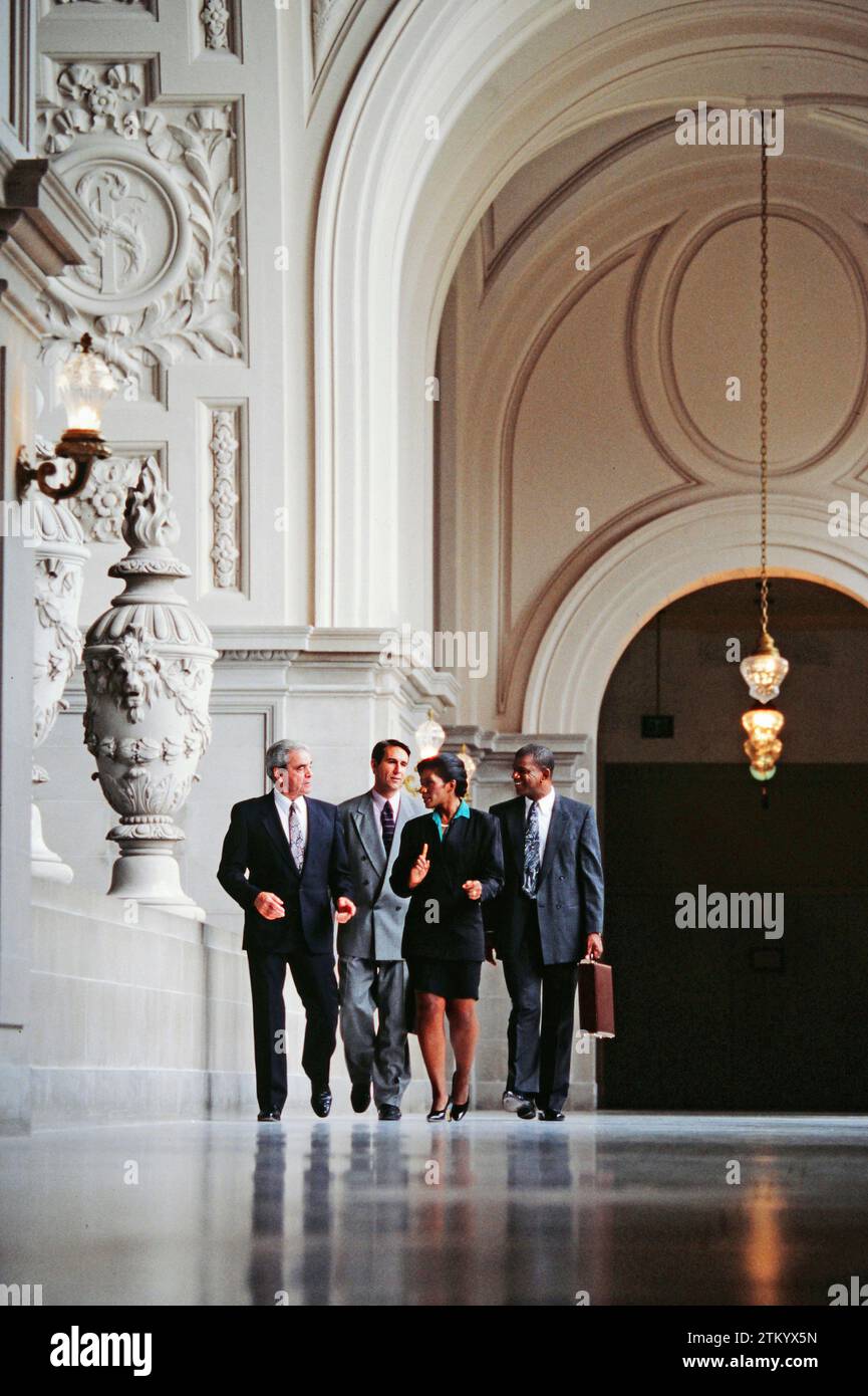 A group of mixed race executives walking together Down the hallway in an ornate building Stock Photo