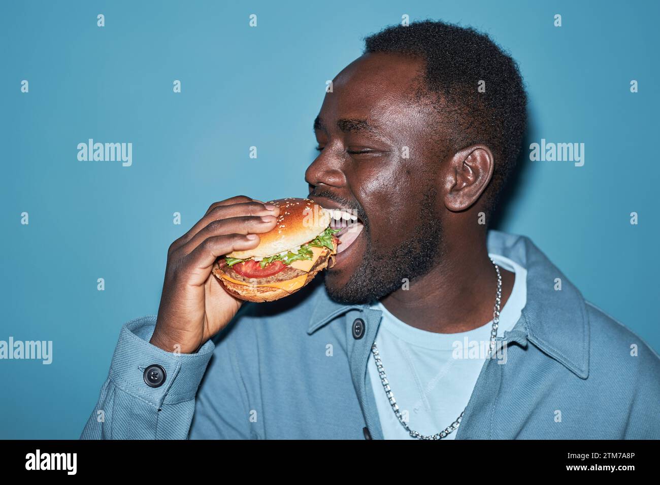 Young Hungry Black Man Eating Burger Stock Photo