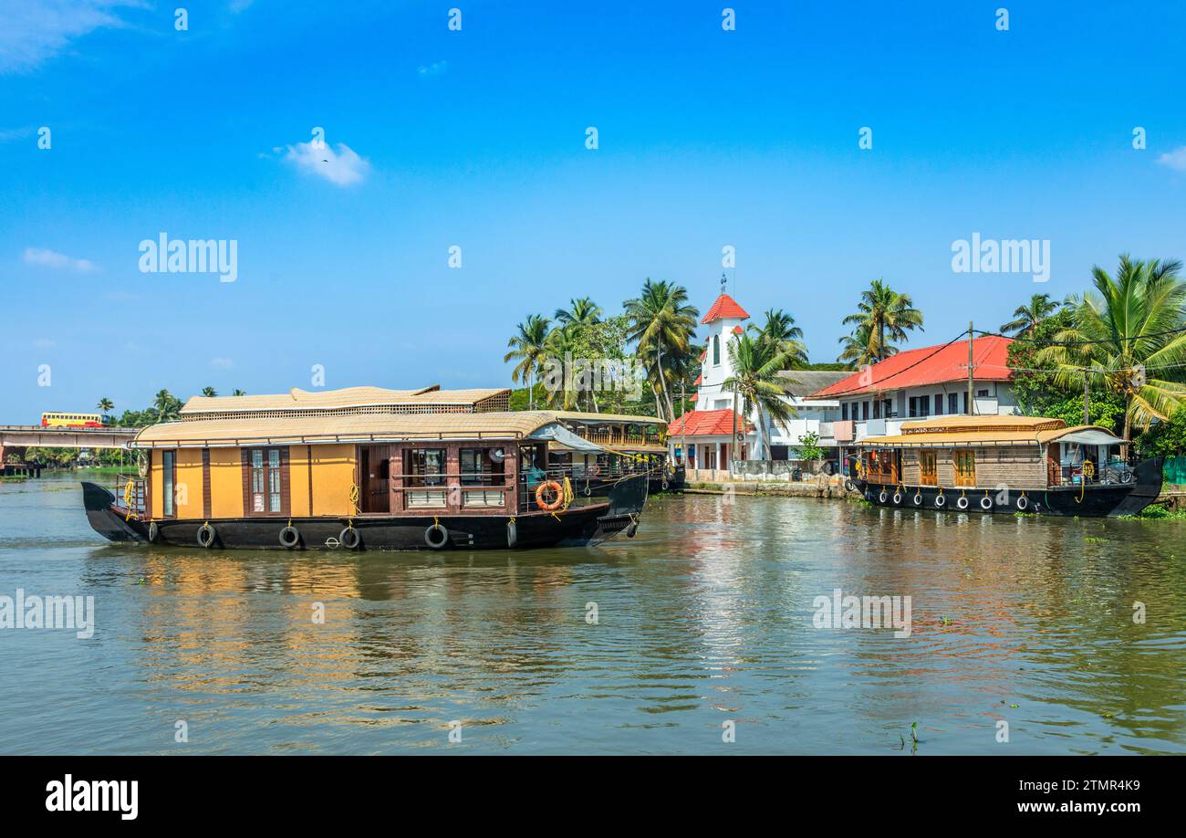 Old colonial Saint Thomas catholic church on the coast of Pamba river, with palms and anchored living houseboats, Alleppey, Kerala, South India Stock Photo