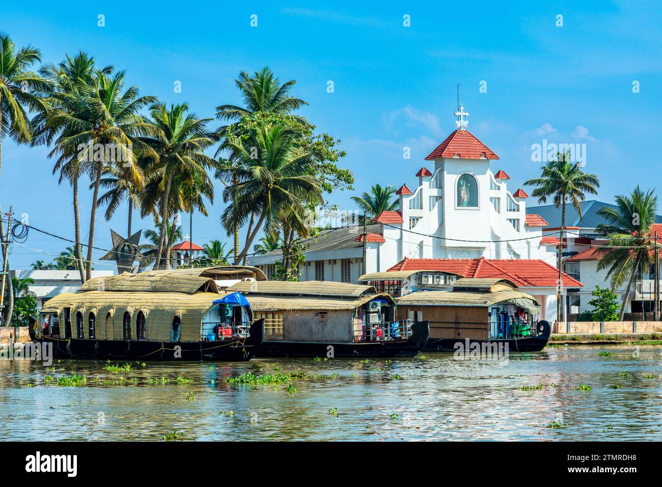 Old colonial Saint Thomas catholic church on the coast of Pamba river, with palms and anchored houseboats, Alleppey, Kerala, South India Stock Photo