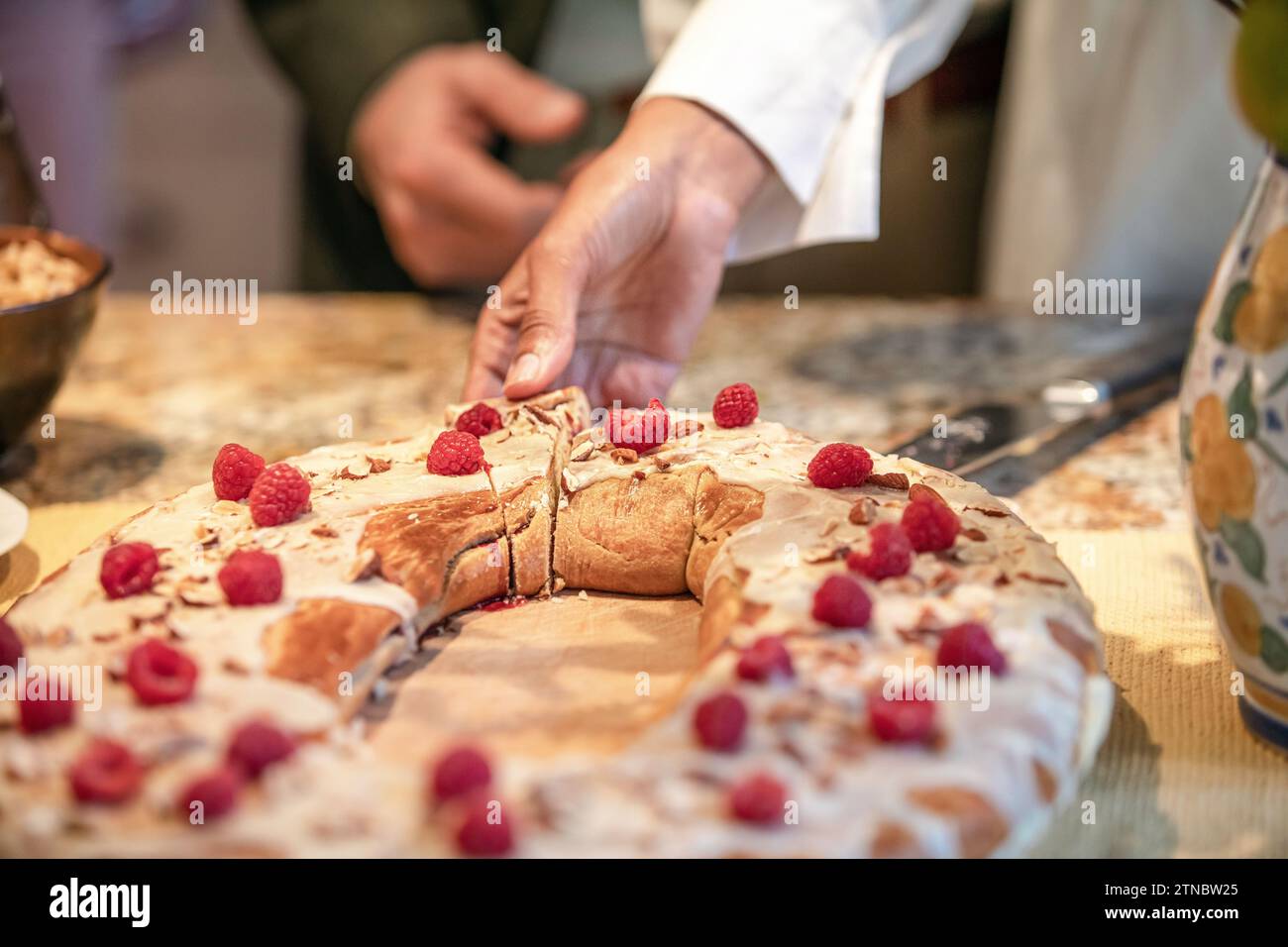 A woman reaches and takes a slice of delicious bread based pastry covered in raspberries and almonds at a wedding reception and tea Stock Photo