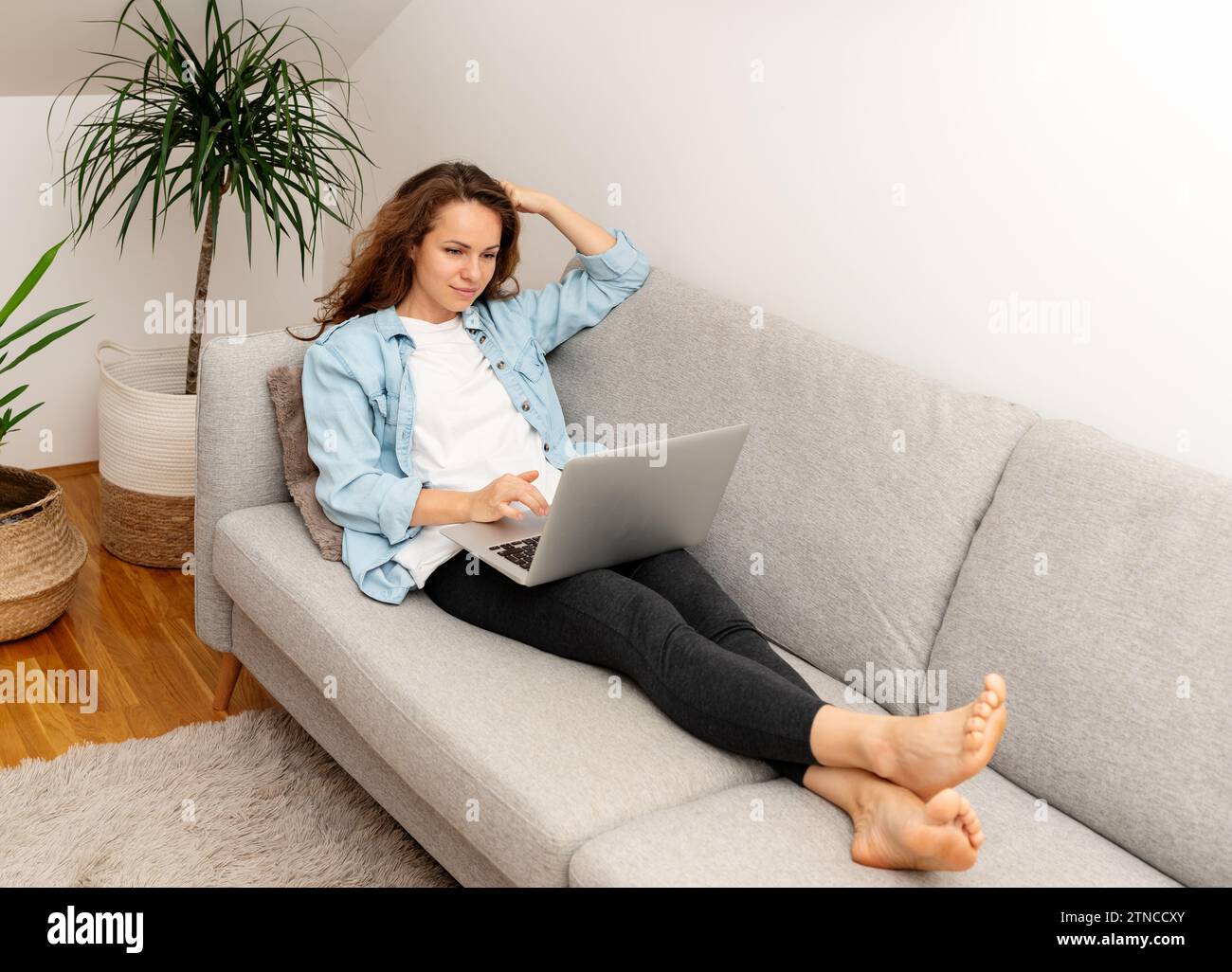 Woman lying on sofa and using her laptop. Stock Photo