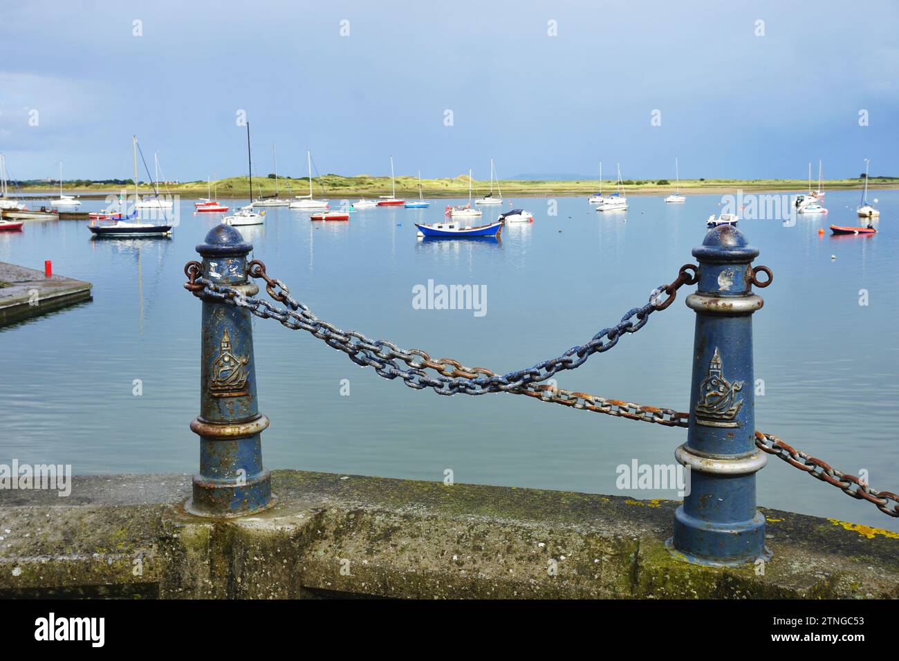 Vintage iron mooring posts frame the view of colorful sailboats at anchor in the protected bay at Malahide Marina on a bright overcast summer day. Stock Photo