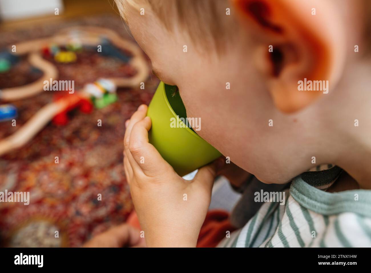 Toddler drinking fresh, clean water from his new plastic green cup, symbolizing healthy habits Stock Photo