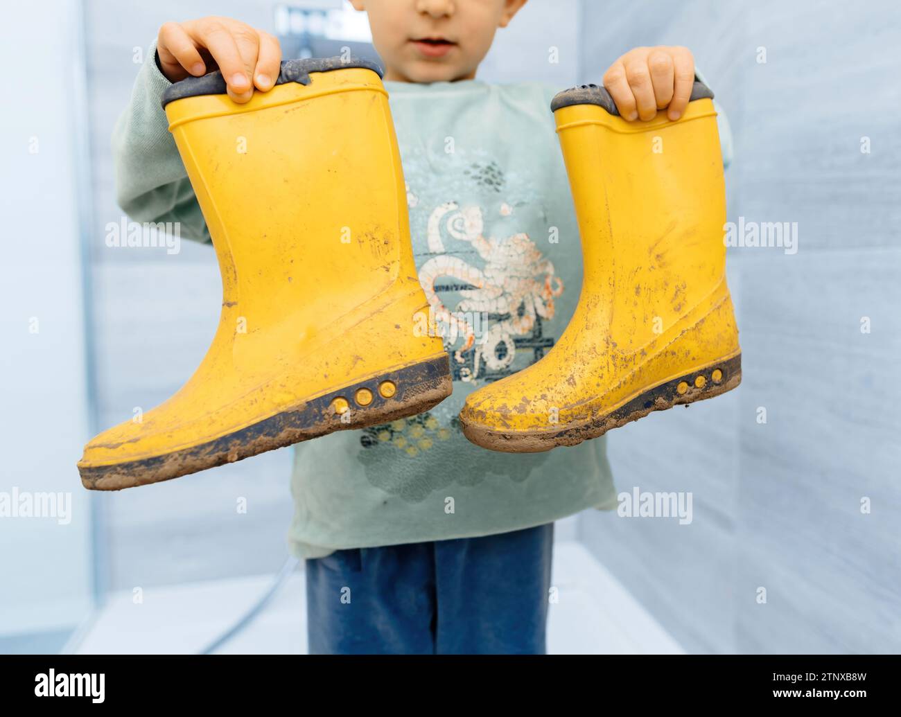 Toddler proudly displaying dirty, mud-covered rubber shoes after an adventurous trail march, showcasing outdoor play Stock Photo