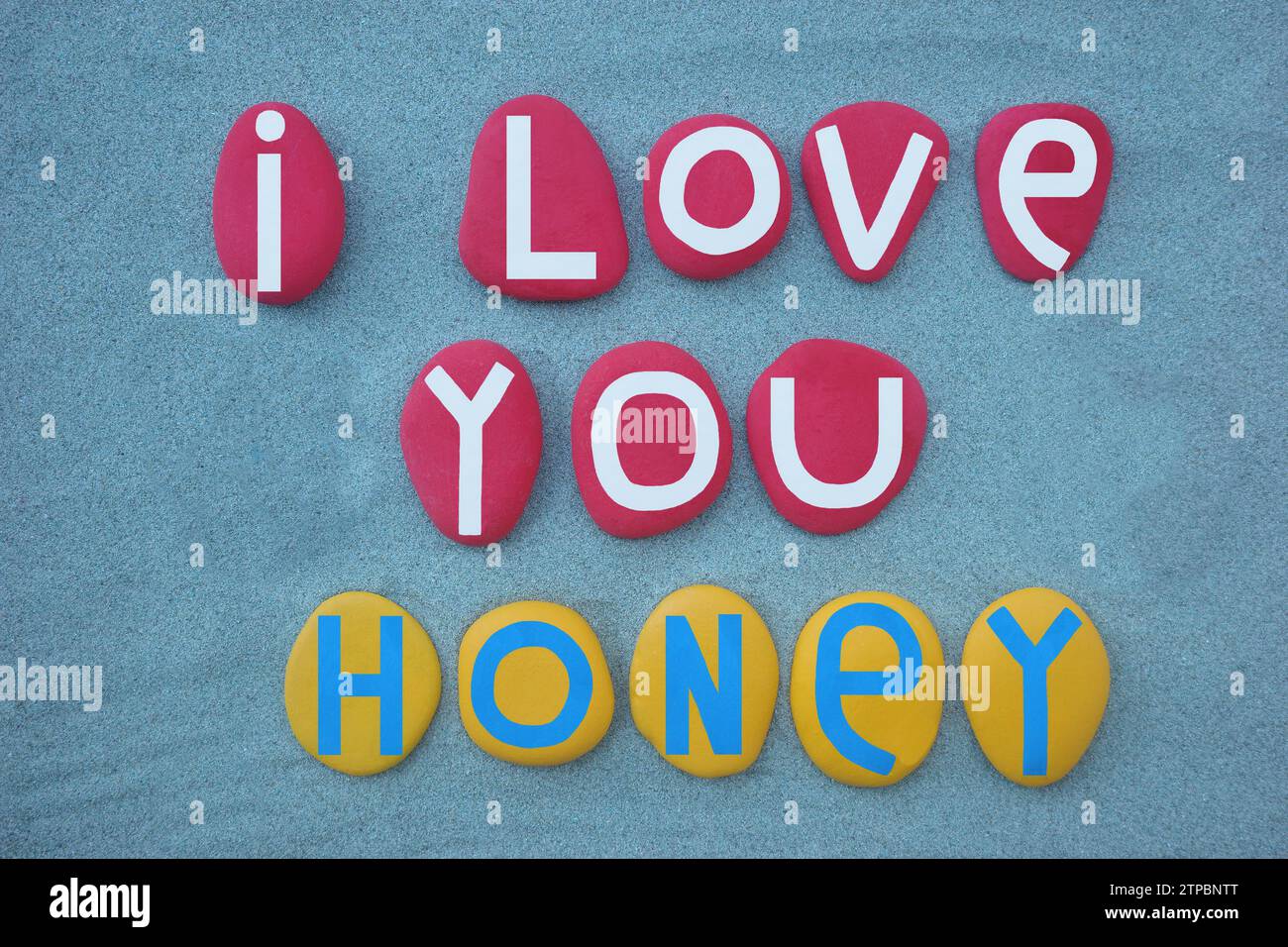 I love you honey, creative message composed with hand painted red and yellow stone letters over green sand Stock Photo