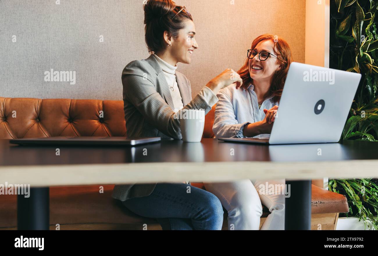 Female colleagues having a discussion while working on a laptop, developing software and utilizing cutting-edge technology. With happy faces, they exe Stock Photo