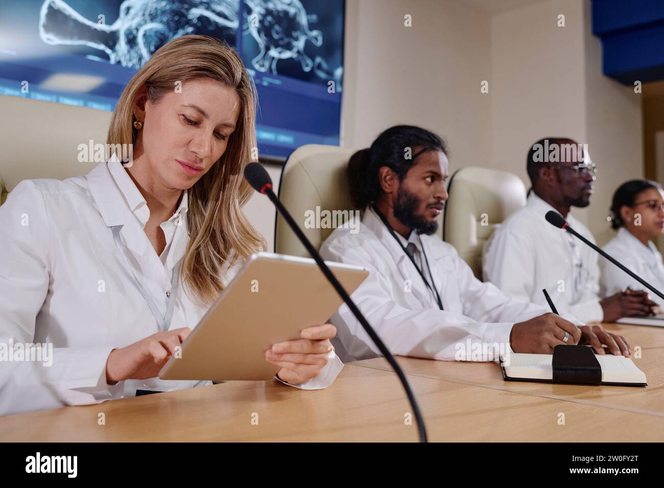 Female doctor using tablet pc while sitting at conference with her colleagues Stock Photo