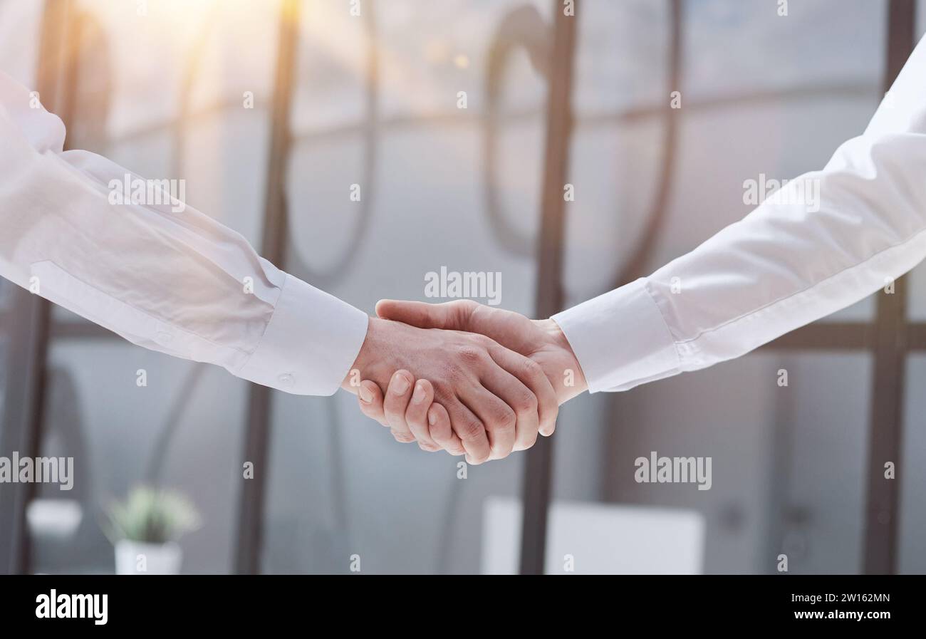 Two businessmen shake hands on the background of empty modern office, signing of a contract concept, close up Stock Photo