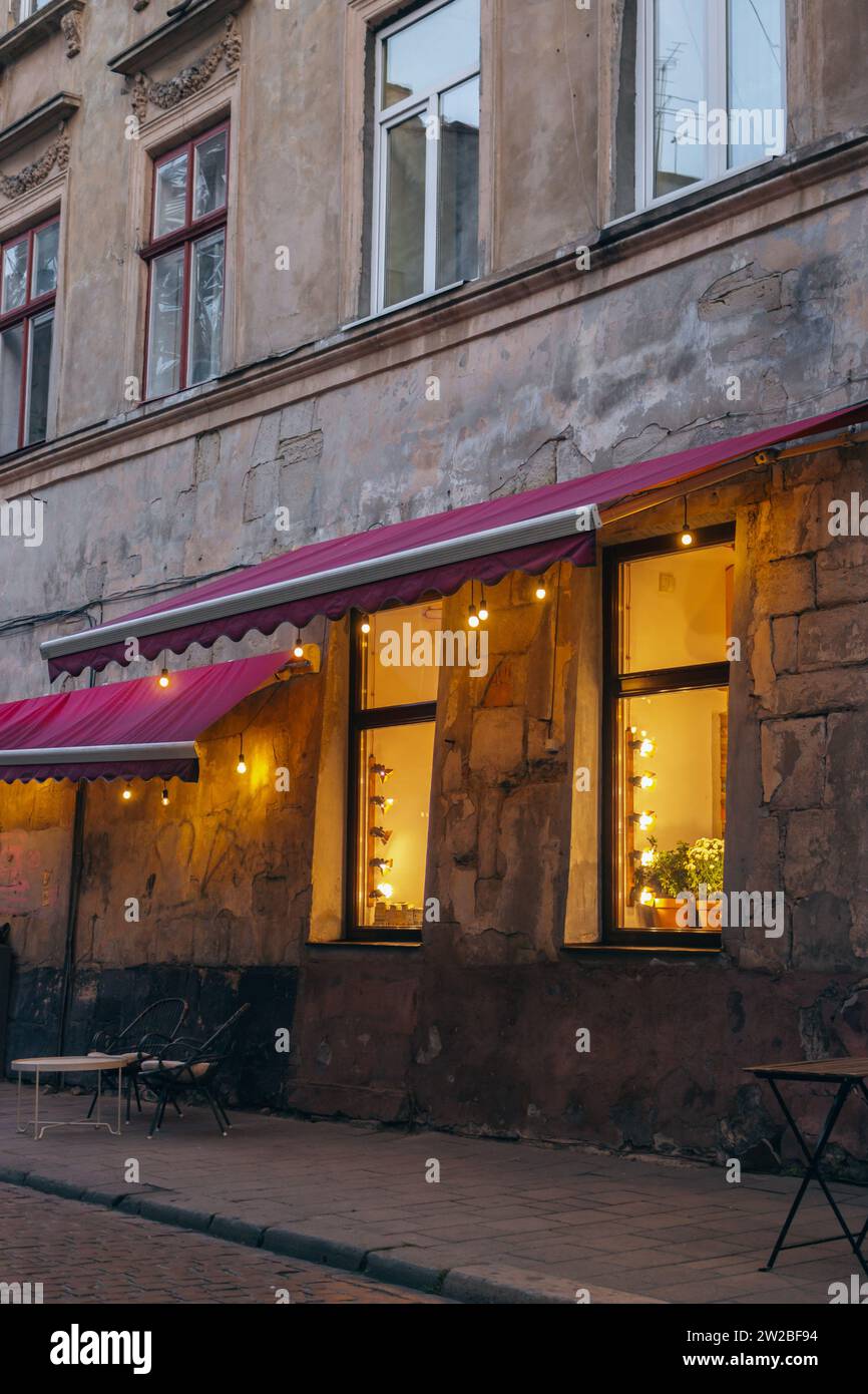 Warm lights in cafe windows in old Lviv town, Ukraine. Sidewalk cafe with outdoor furniture and garland in windows. Sidewalk cafe in ancient house Stock Photo