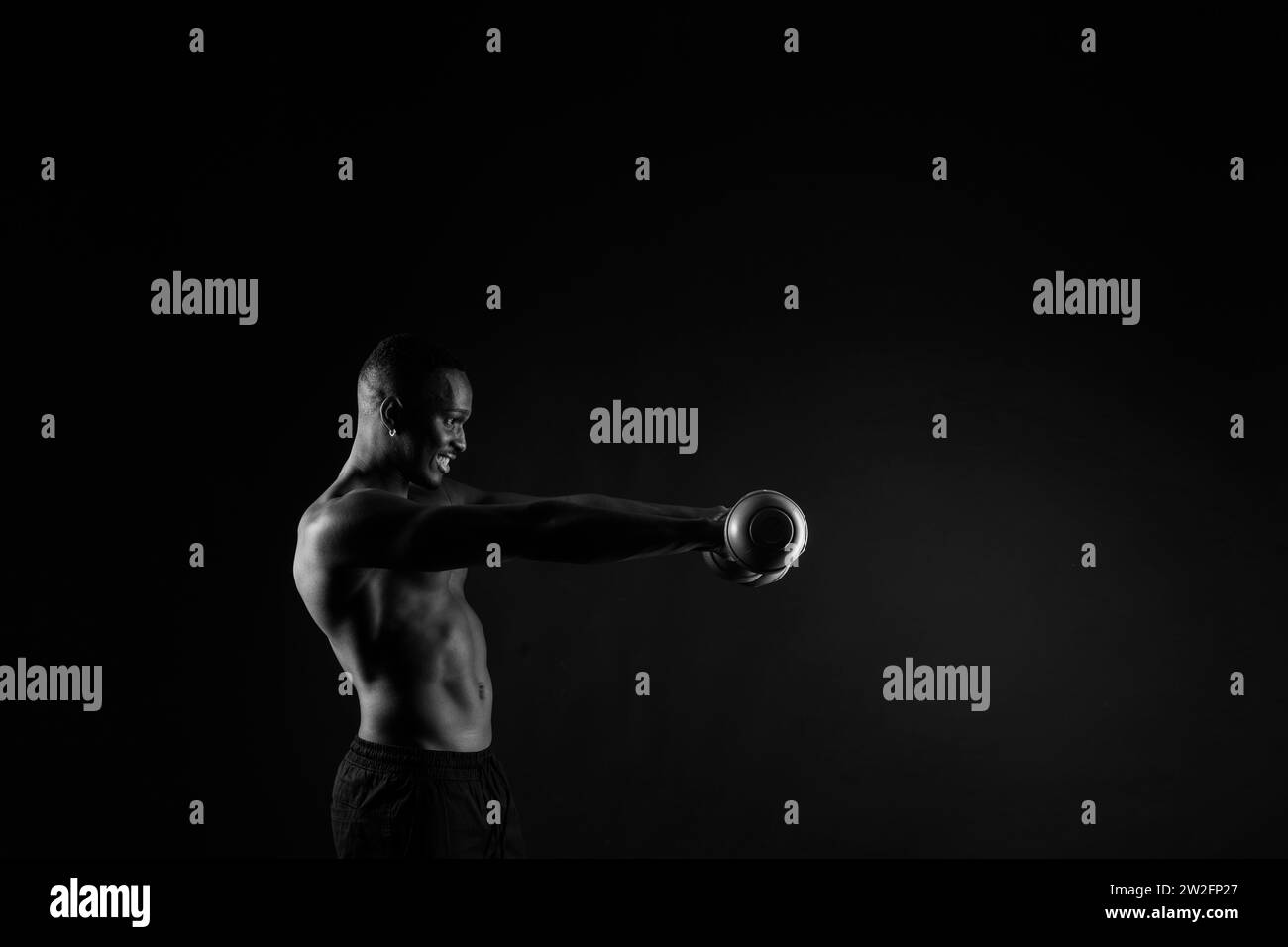 Young man with dumbbells good physique isolated on red and black background. Strength and motivation Stock Photo