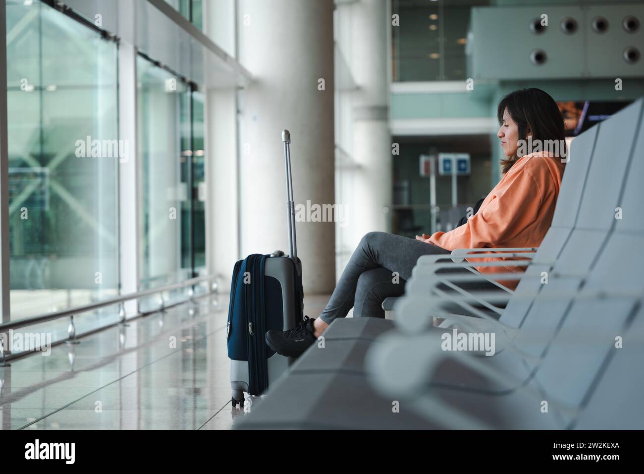 Seated woman, looks through the airport window, waiting for her flight. Stock Photo