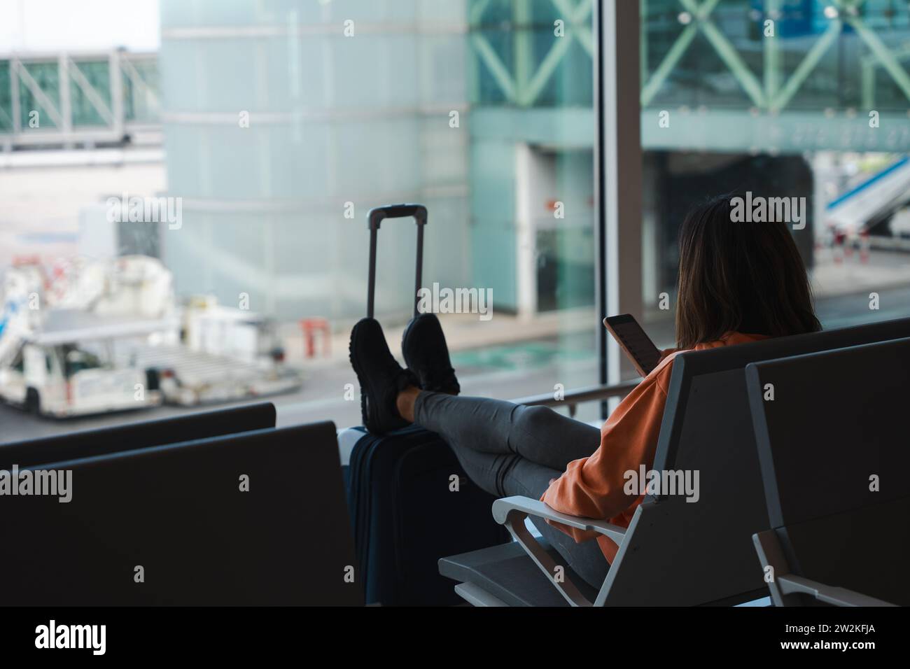 Woman checks her mobile phone while waiting for her flight at the airport. Stock Photo