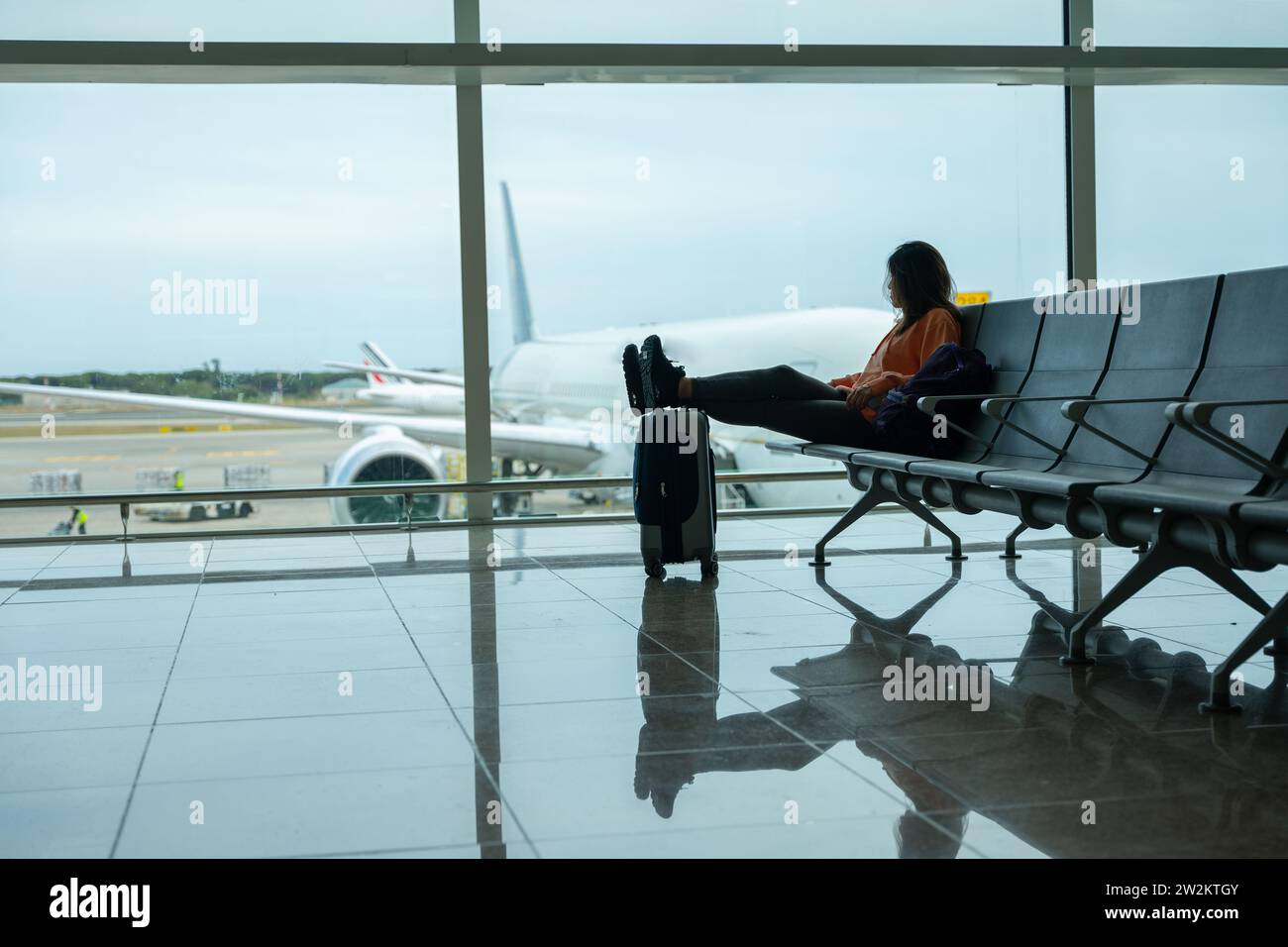 Woman with her feet on her suitcase, waiting for her flight at the airport. Stock Photo