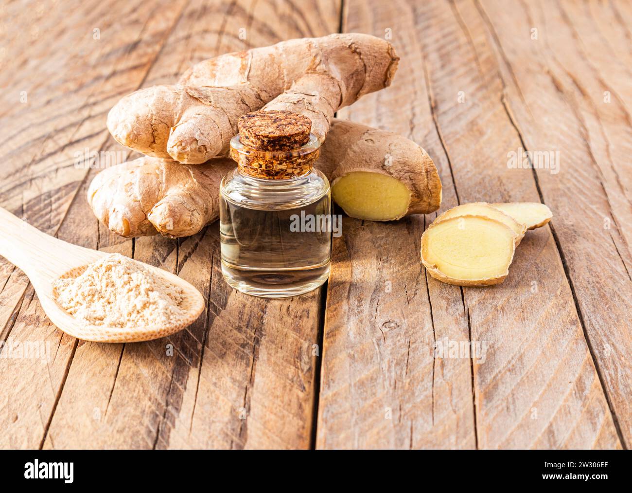 Ginger root essential oil in a glass bottle with a cork cap on a wooden table with root . Skin rejuvenation, strengthening hair growth Stock Photo