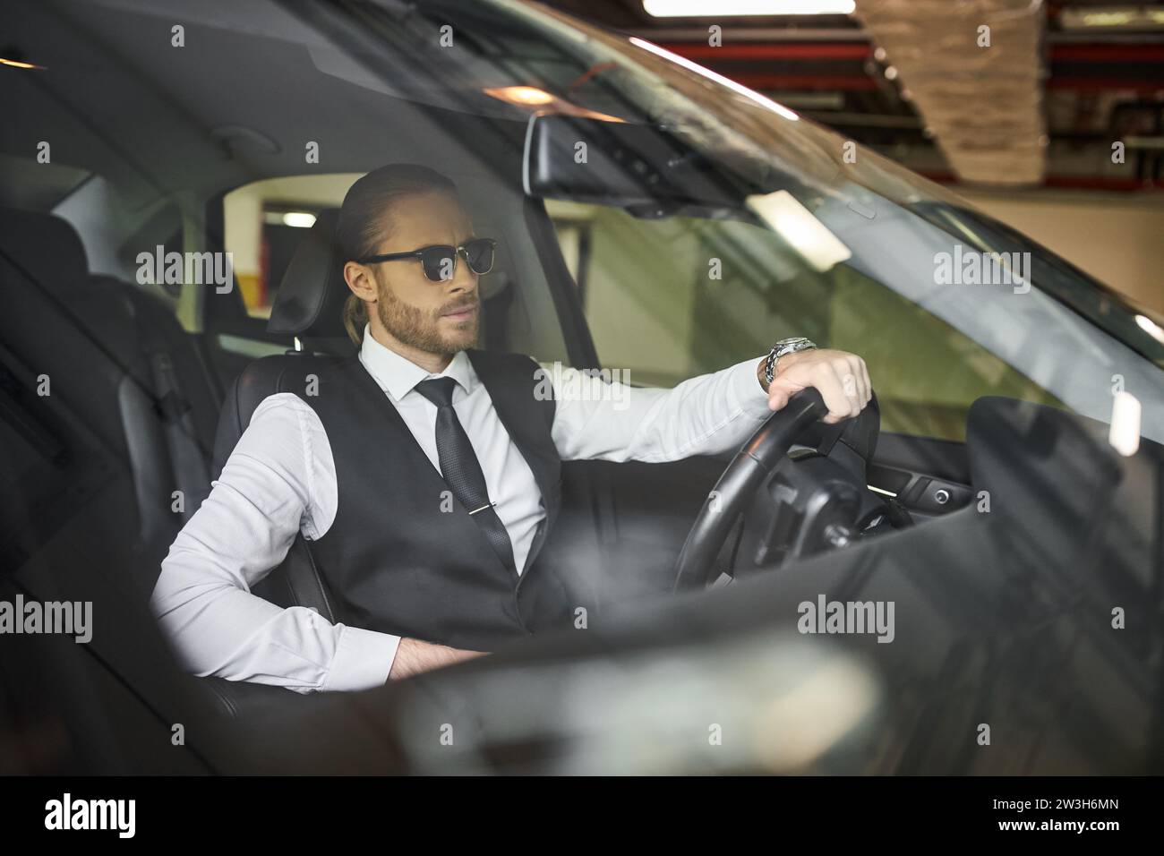 handsome bearded businessman with exquisite dapper style with sunglasses behind steering wheel Stock Photo