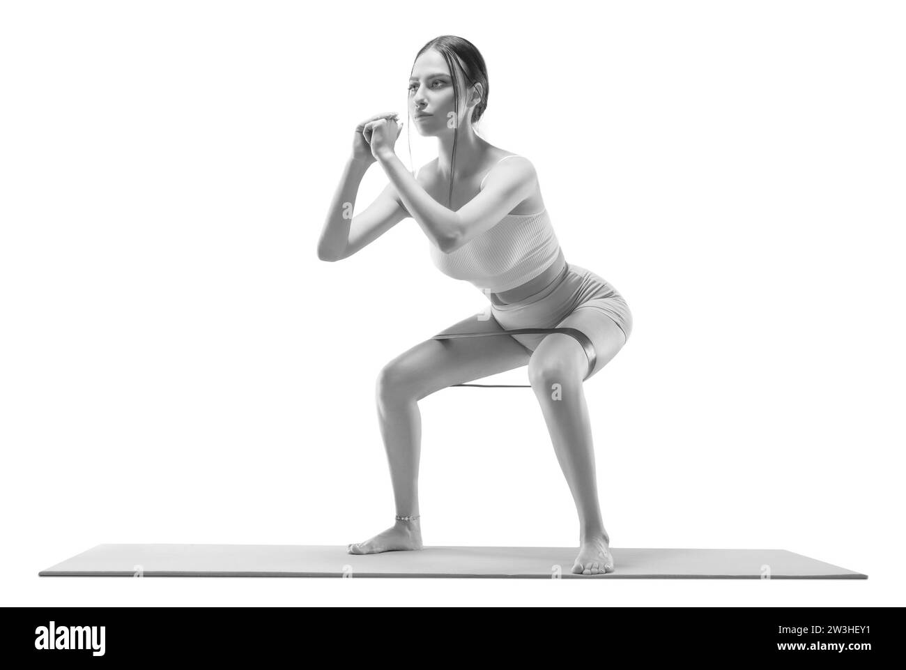 Image of an athletic girl squatting with an elastic band on a mat. The concept of shaping, pilates, stretching. Mixed media Stock Photo