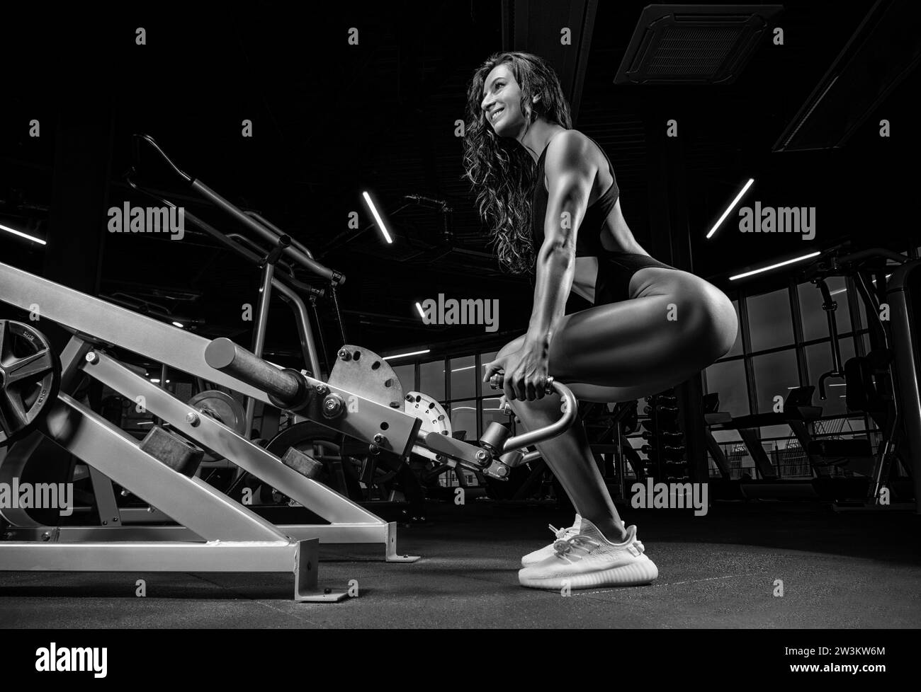 Tall athletic woman squats in the gym in a special apparatus. Deadlift. Fitness and bodybuilding concept. Mixed media Stock Photo