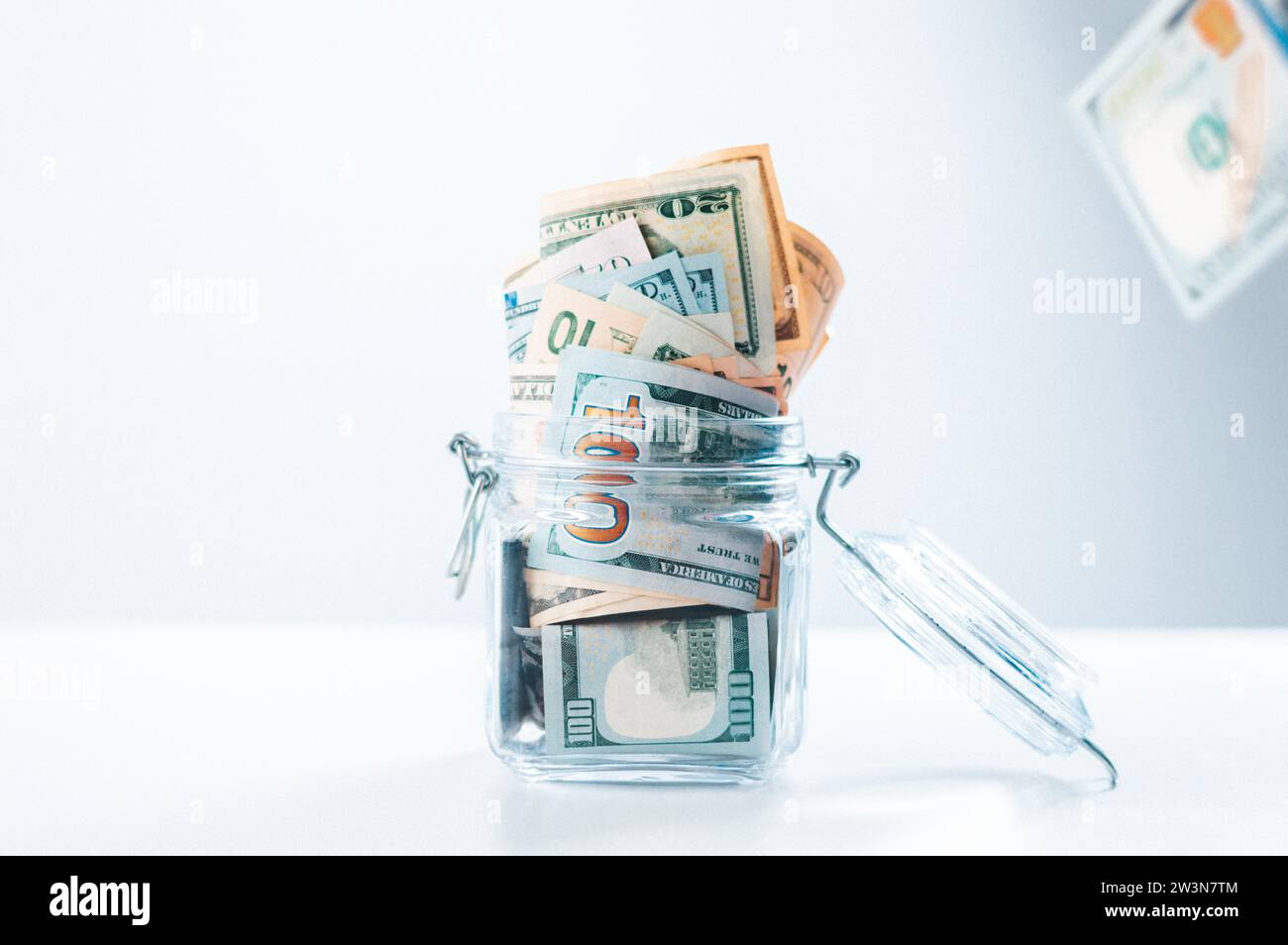 Glass piggy bank full of money. Banknotes are strewed from above. The concept of squandering. Mixed media Stock Photo