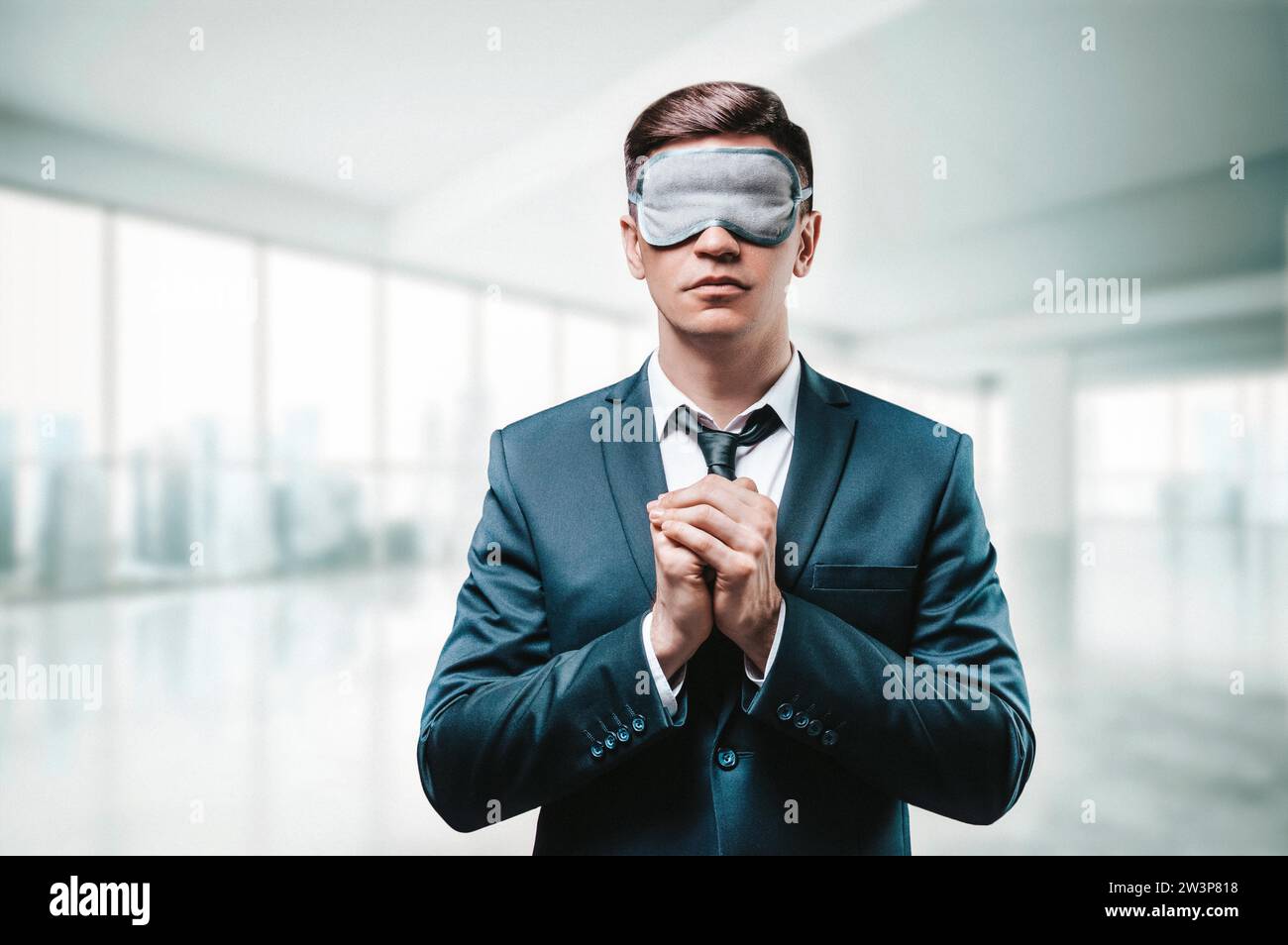 Portrait of a man in a business suit. He is praying while standing in the office. He has a sleep mask on his eyes. Blind business concept. Mixed media Stock Photo
