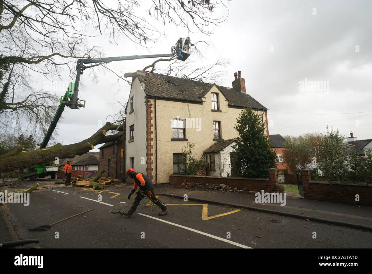 Workmen remove a fallen tree which has damaged the roof of a house in