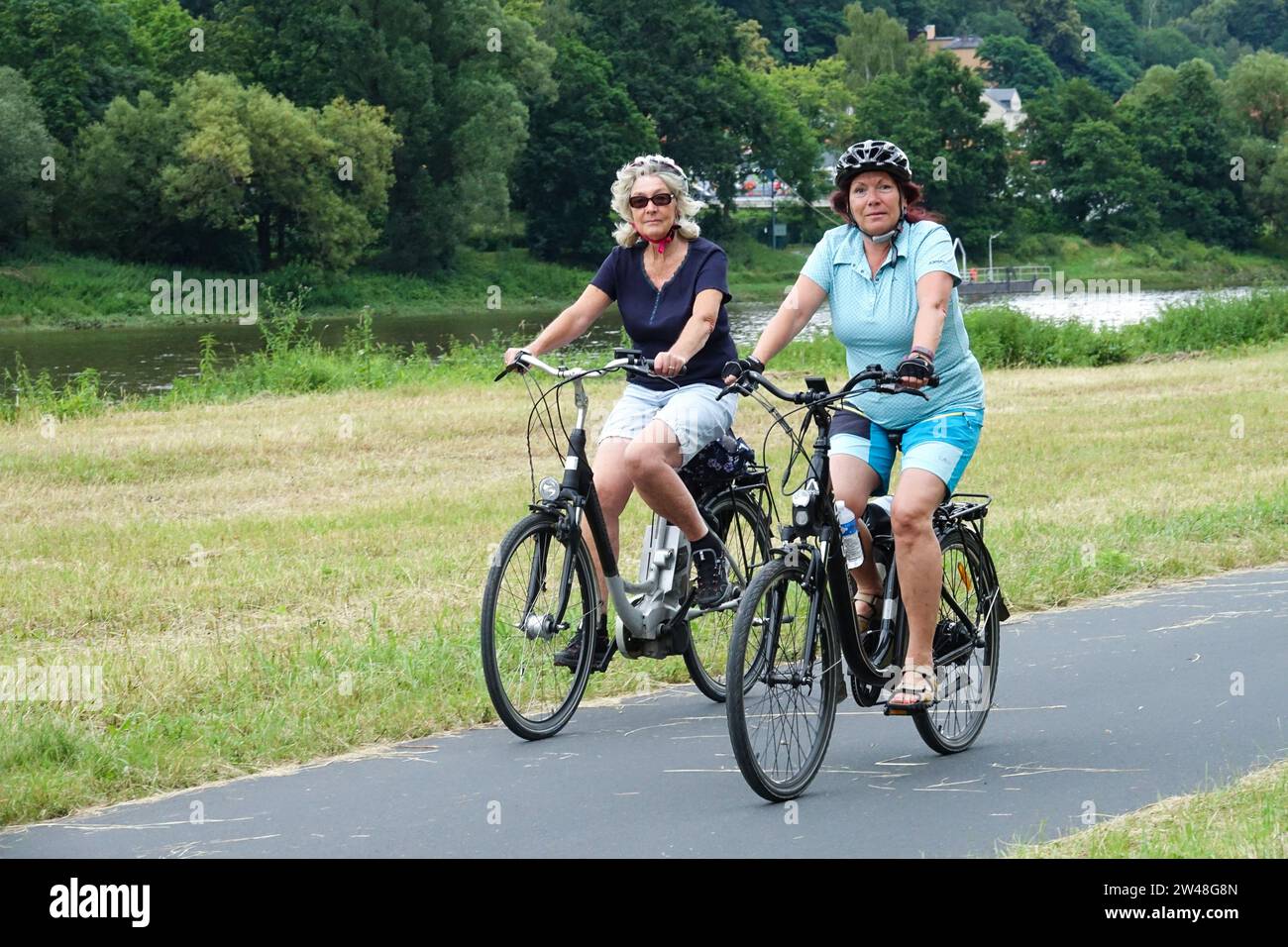 Two senior women ride a bicycle on a cycle path along the river Elbe Saxony Germany Stock Photo