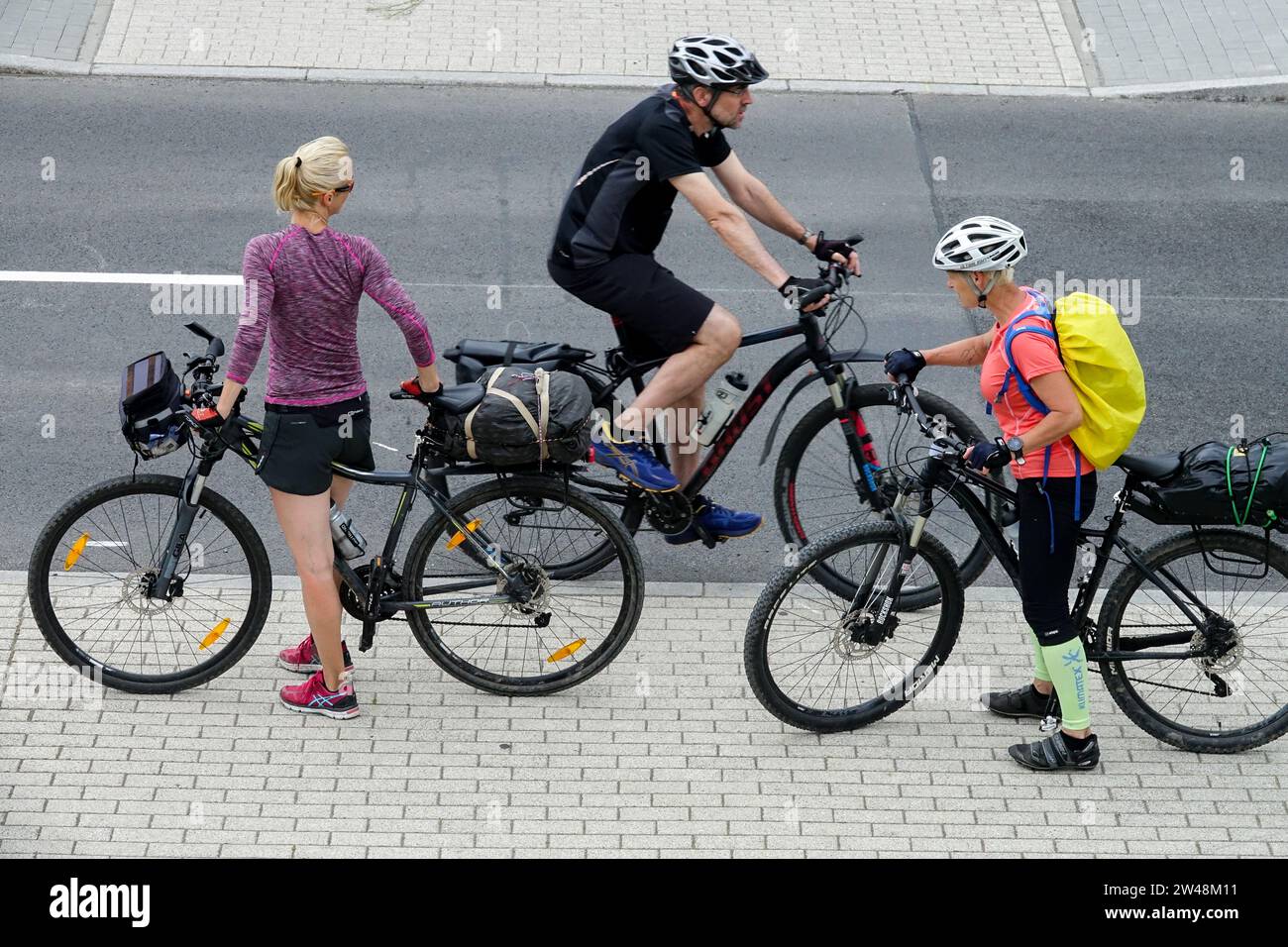 Two women on bicycles meet a passing man on a bicycle Stock Photo