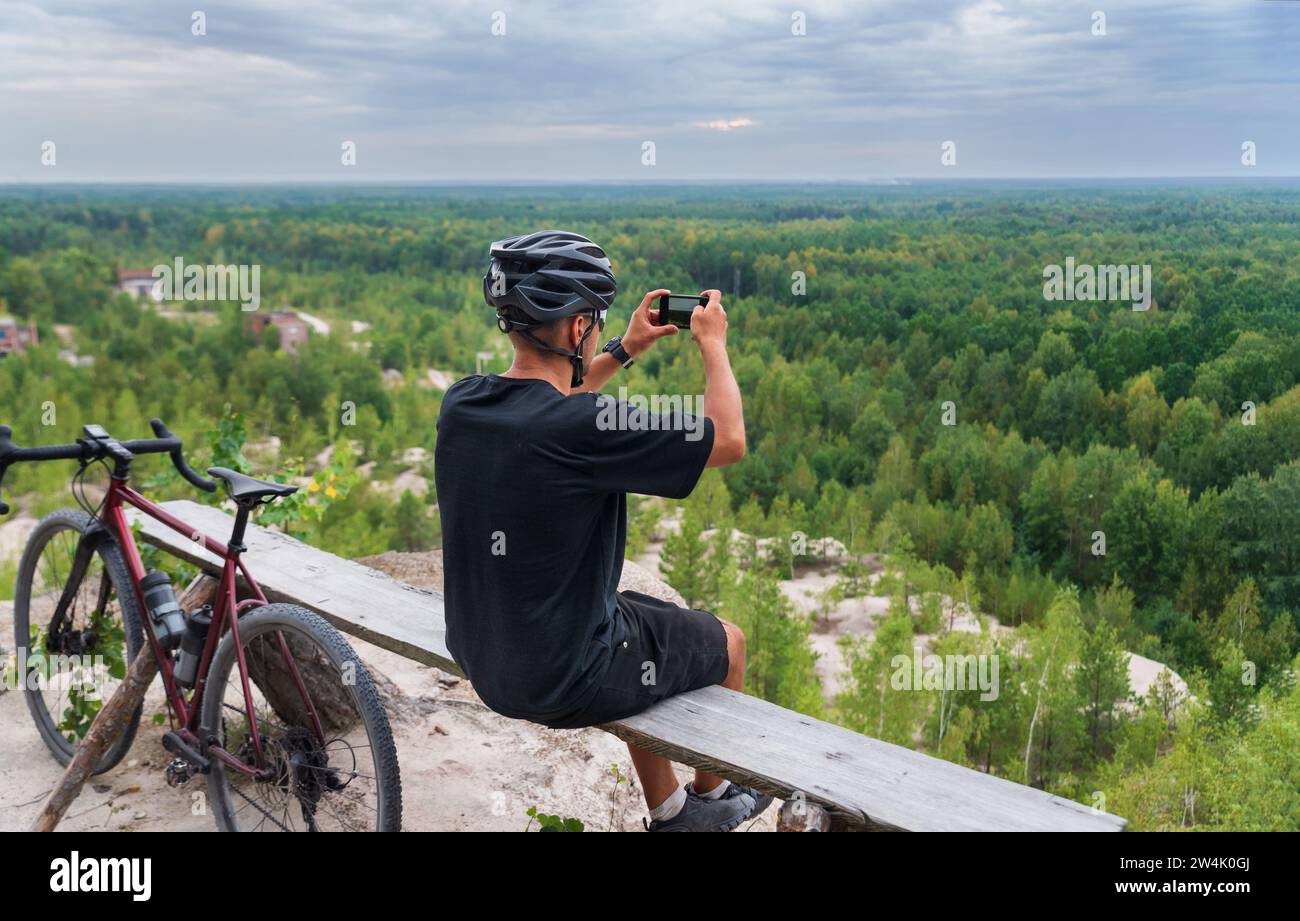 A cyclist takes pictures of a beautiful landscape on his mobile phone while training on a bicycle. Sport and travel. Stock Photo