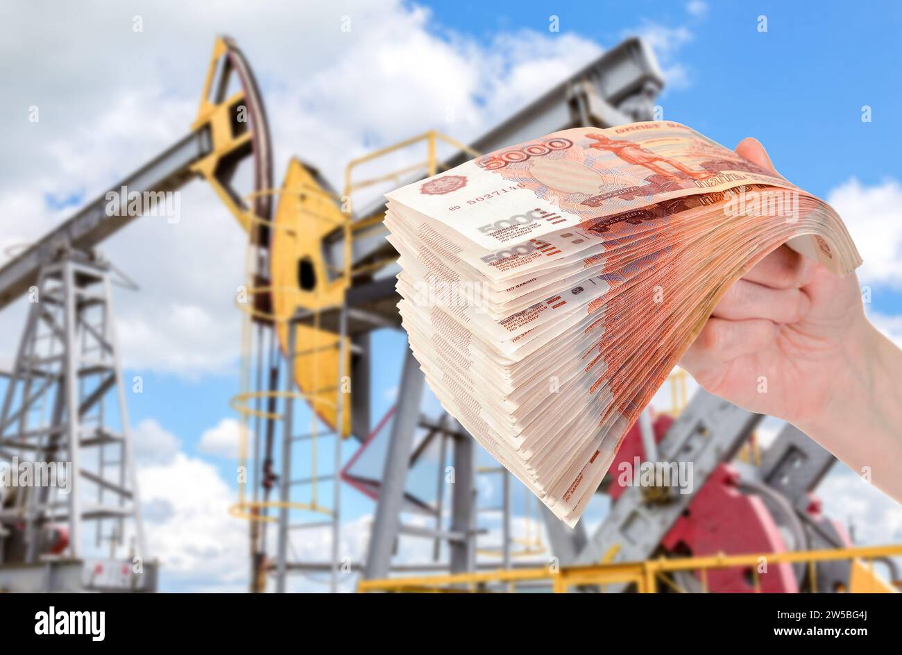 Russian roubles in the hand against the oil pump jack extraction machine. Buying and selling oil for rubles. Oil industry equipment and finace Stock Photo