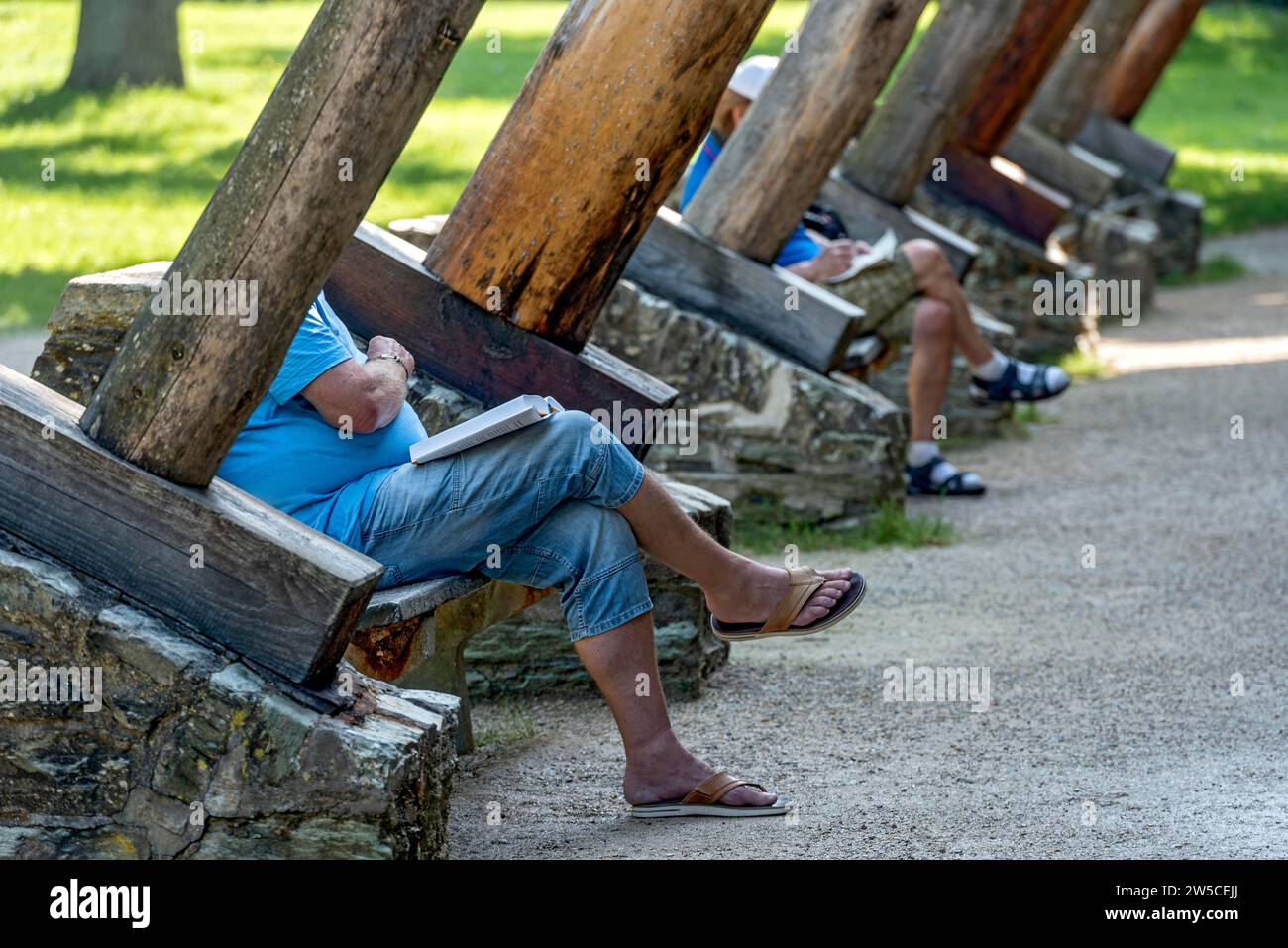 Men relaxing on benches between supporting beams of Gradierbau I, graduation house, open-air inhalatorium, salty aerosols for relaxation, healing of Stock Photo