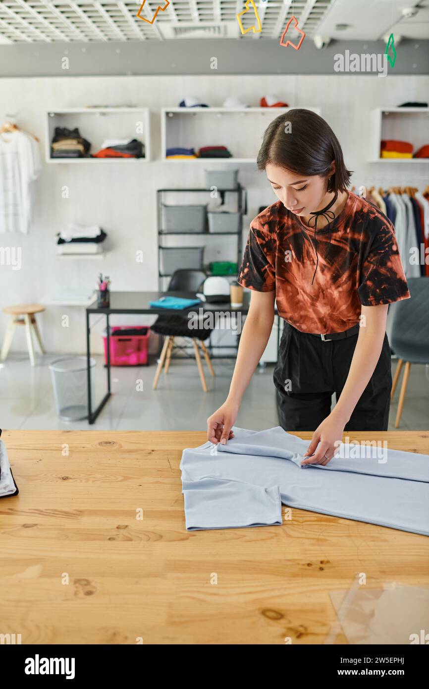 young and stylish asian woman folding clothes on table in print