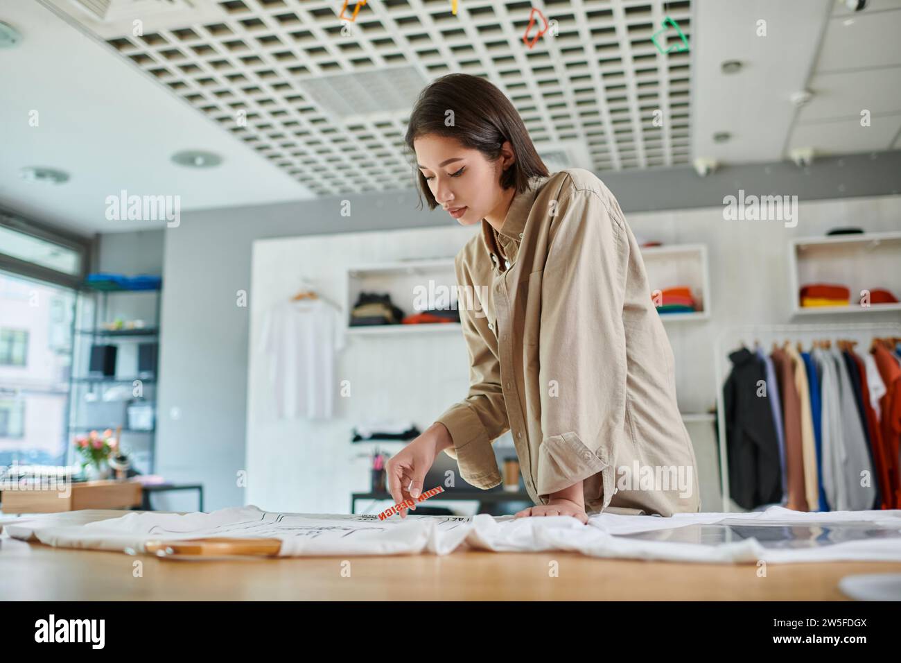 thoughtful female asian designer holding text template near clothing in ...