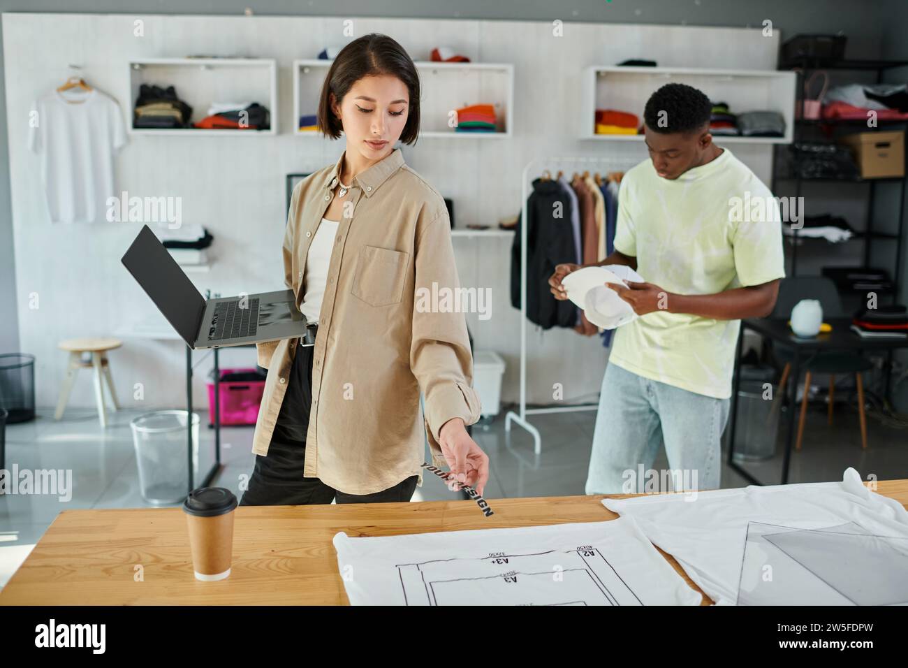 asian designer with laptop and text template near clothes and african american man in print studio Stock Photo