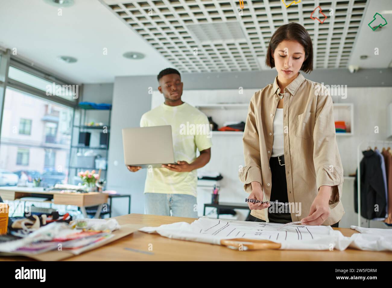 asian designer holding text templates near african american colleague with laptop in print studio Stock Photo