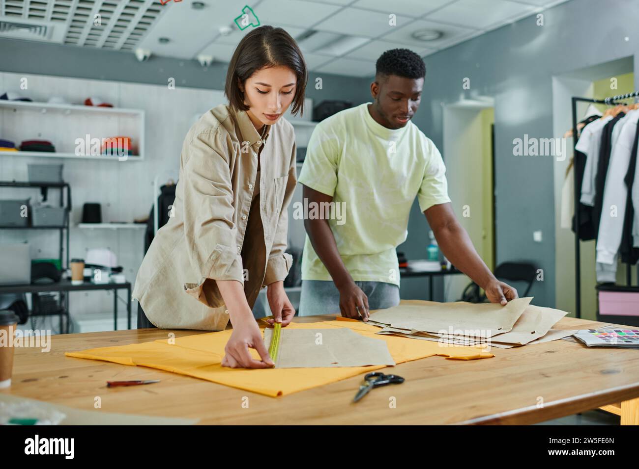 skilled interracial fashion designers measuring sewing patterns in print studio, small business Stock Photo
