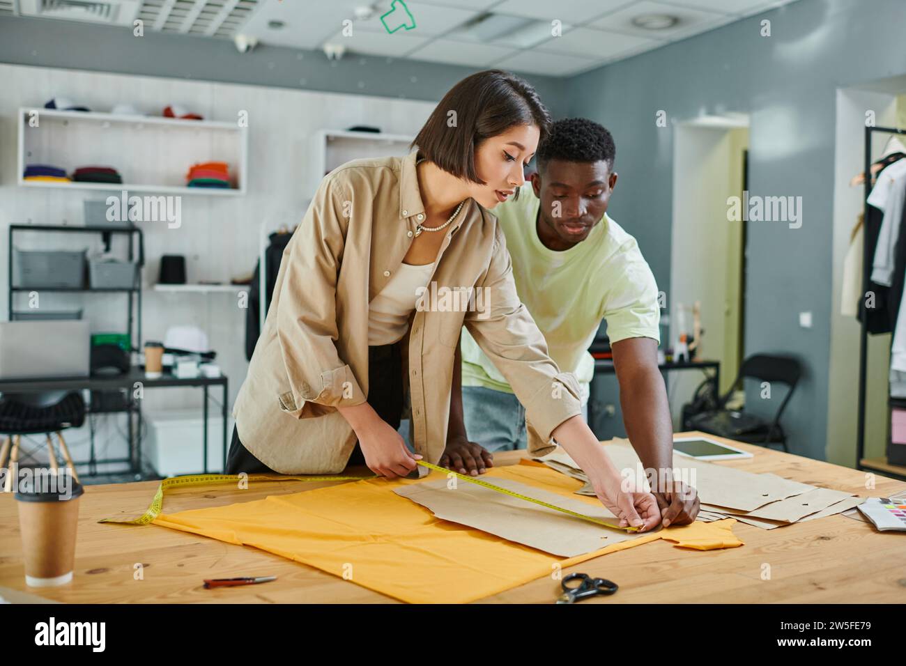 young interracial fashion designers measuring sewing patterns in print studio, creative teamwork Stock Photo