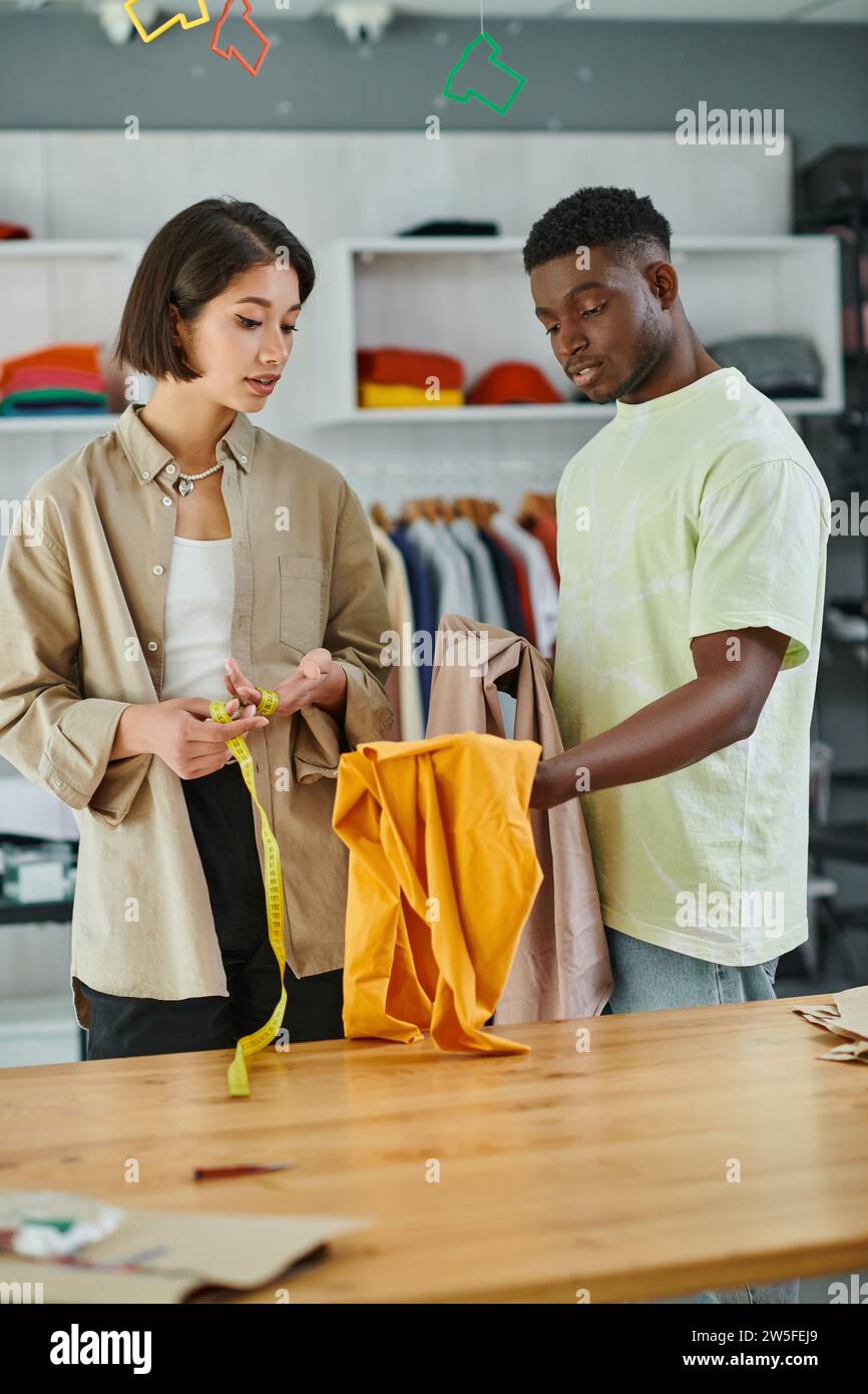 multicultural fashion designers holding fabric and measuring tape in print studio, teamwork Stock Photo