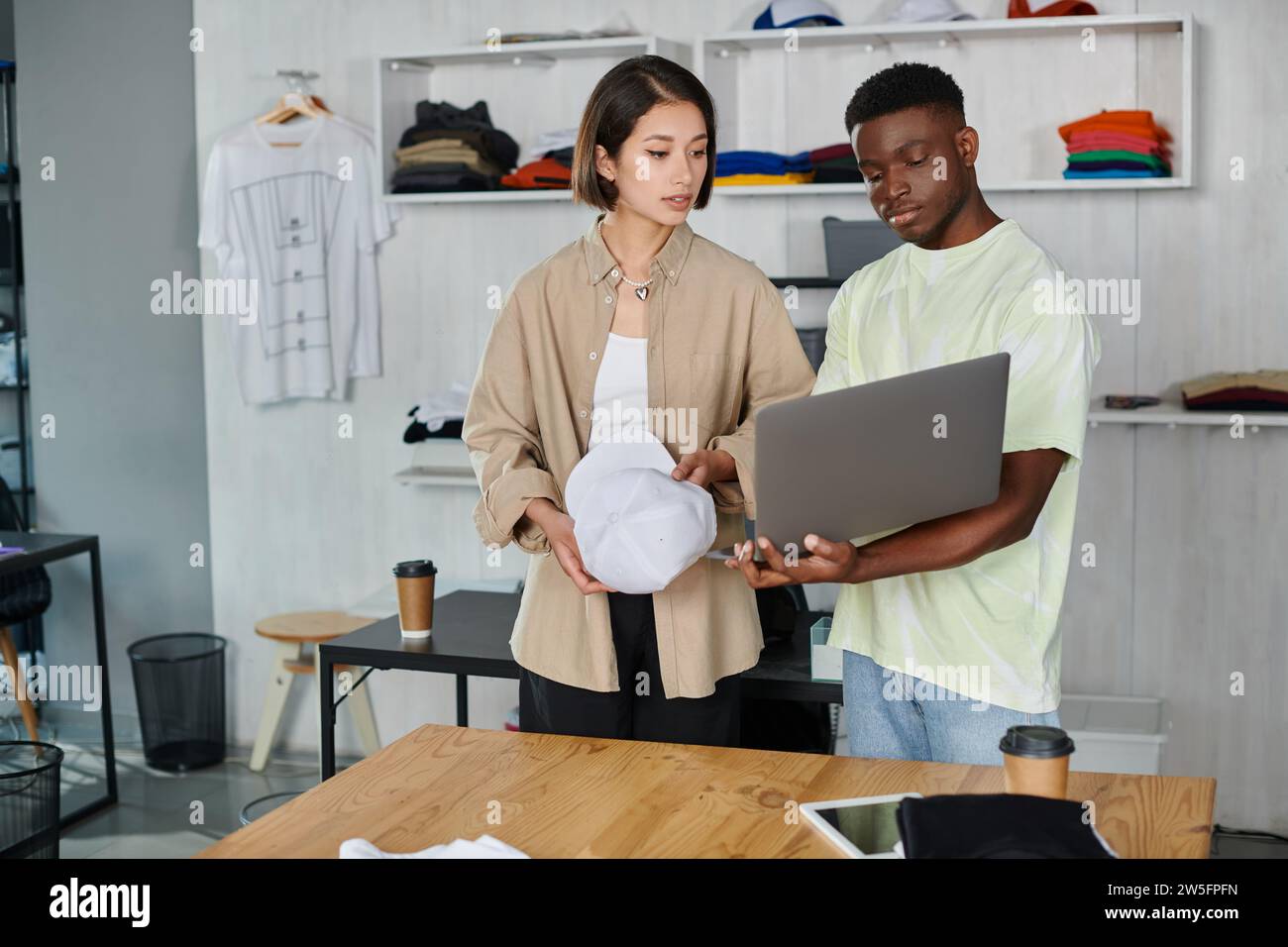 creative african american designer showing laptop to asian woman with white cap in print studio Stock Photo