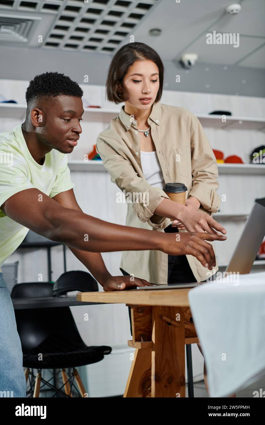 multiethnic designers pointing at laptop while working on new project in textile printing workshop Stock Photo