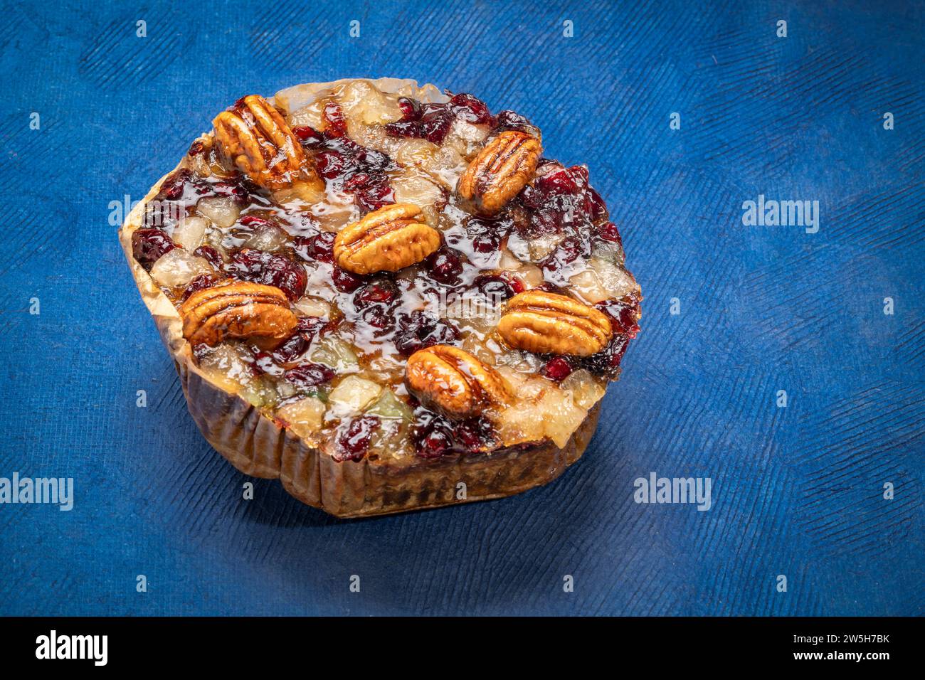 holiday rum cake with pecans, pineapple, dried cherries and cranberries against blue art paper Stock Photo
