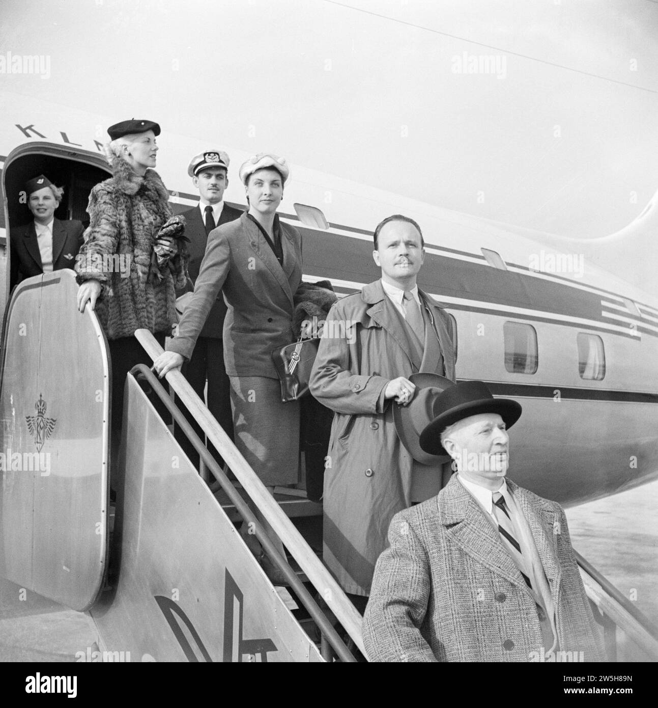 Passengers disembark from a KLM passenger plane via the stairs under the watchful eye of a KLM purser and stewardess ca. 1950 Stock Photo