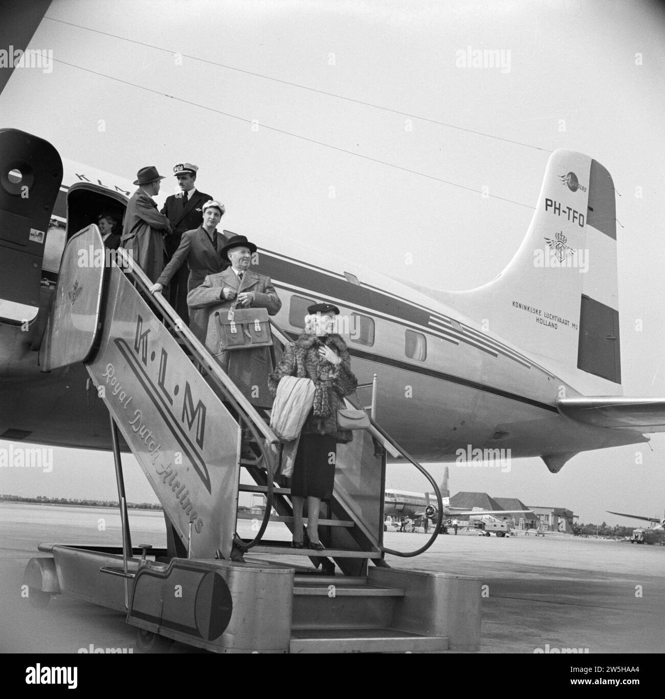 Passengers disembark from a KLM passenger plane via the stairs under the watchful eye of a KLM purser and stewardess ca. 1950 Stock Photo