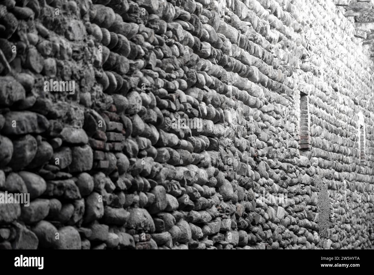 A stone wall made of coarse natural stone or fieldstone with small windows. The picture is rather colorless. Stock Photo