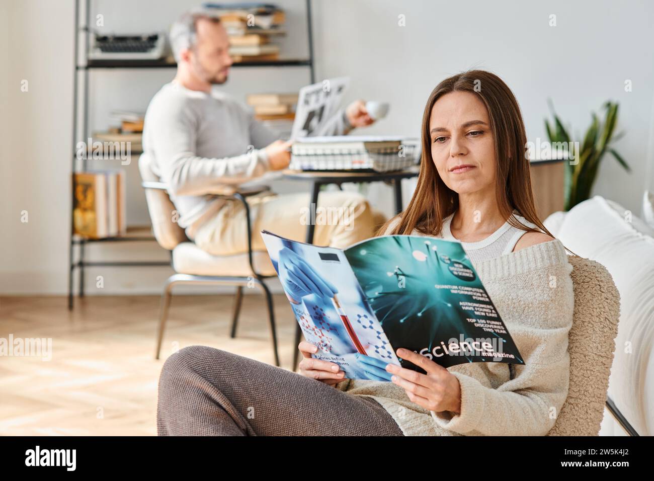 focused woman reading science magazine near husband in living room ...