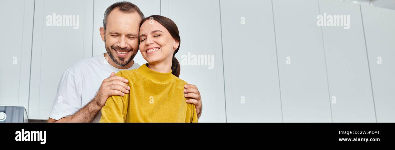 loving husband with closed eyes embracing shoulders of happy wife in  kitchen, horizontal banner Stock Photo