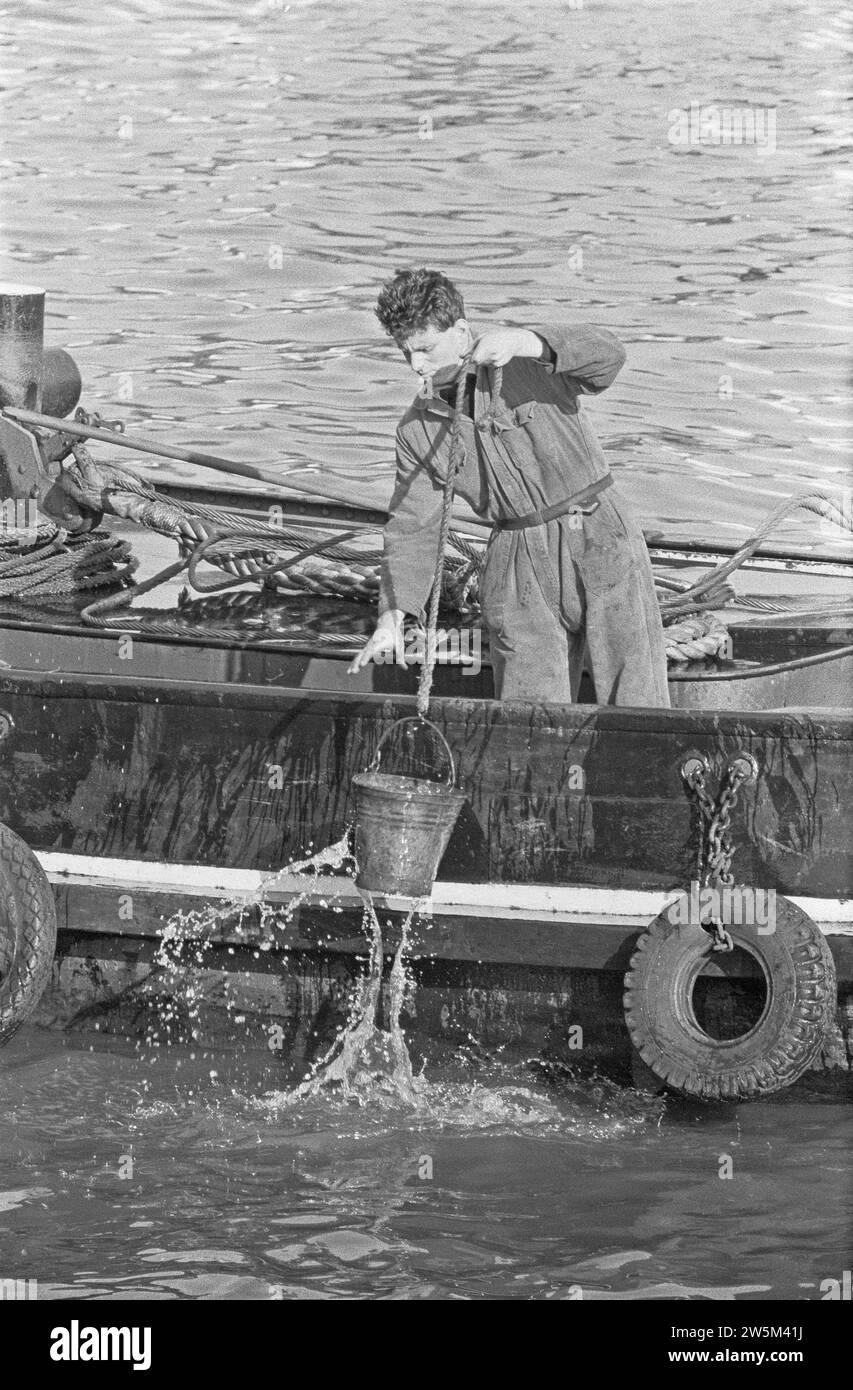 Man working on a boat pulling up a pail of water in the port of