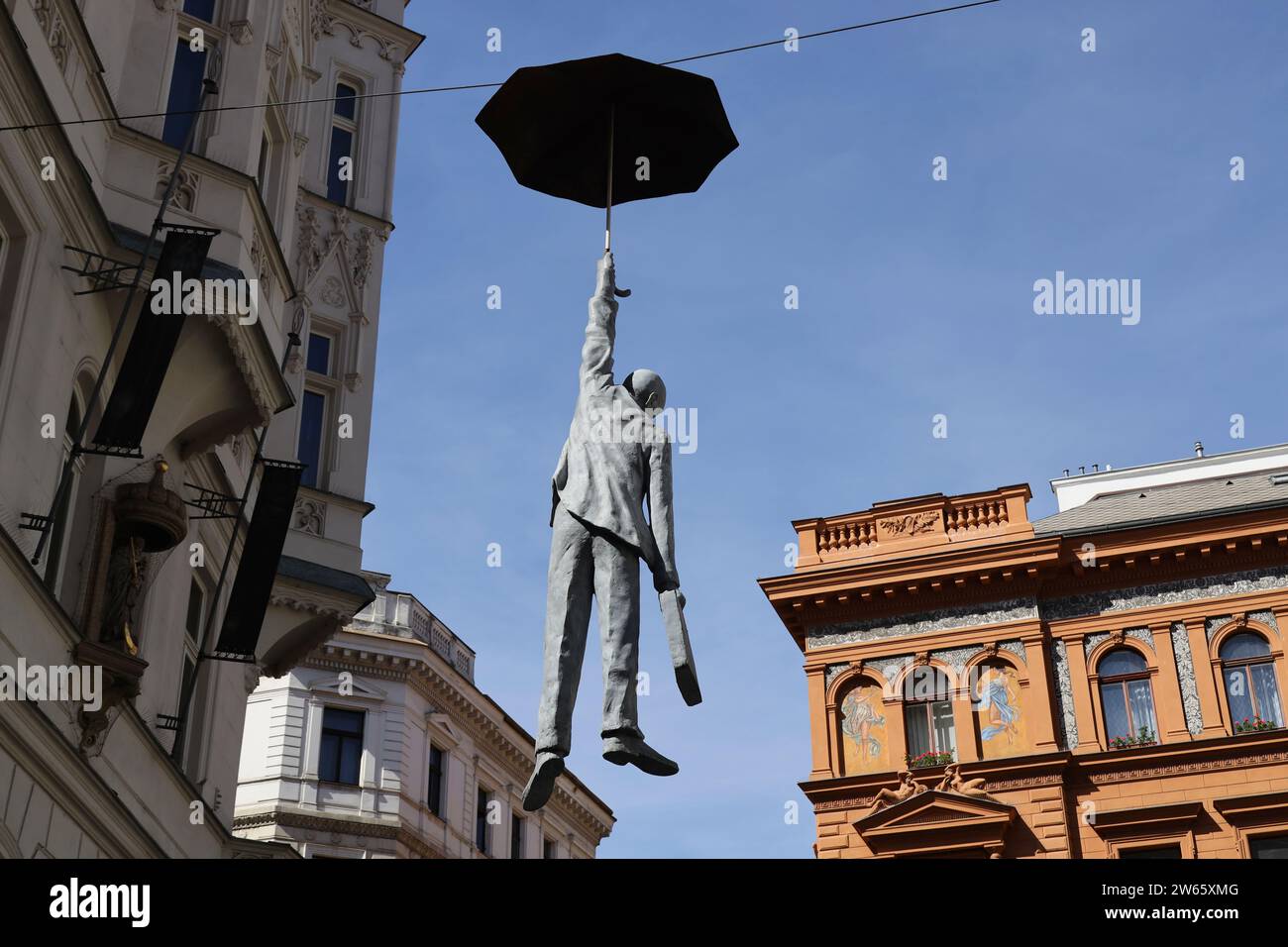 Sculpture of man hanging from an umbrella suspended high above a street